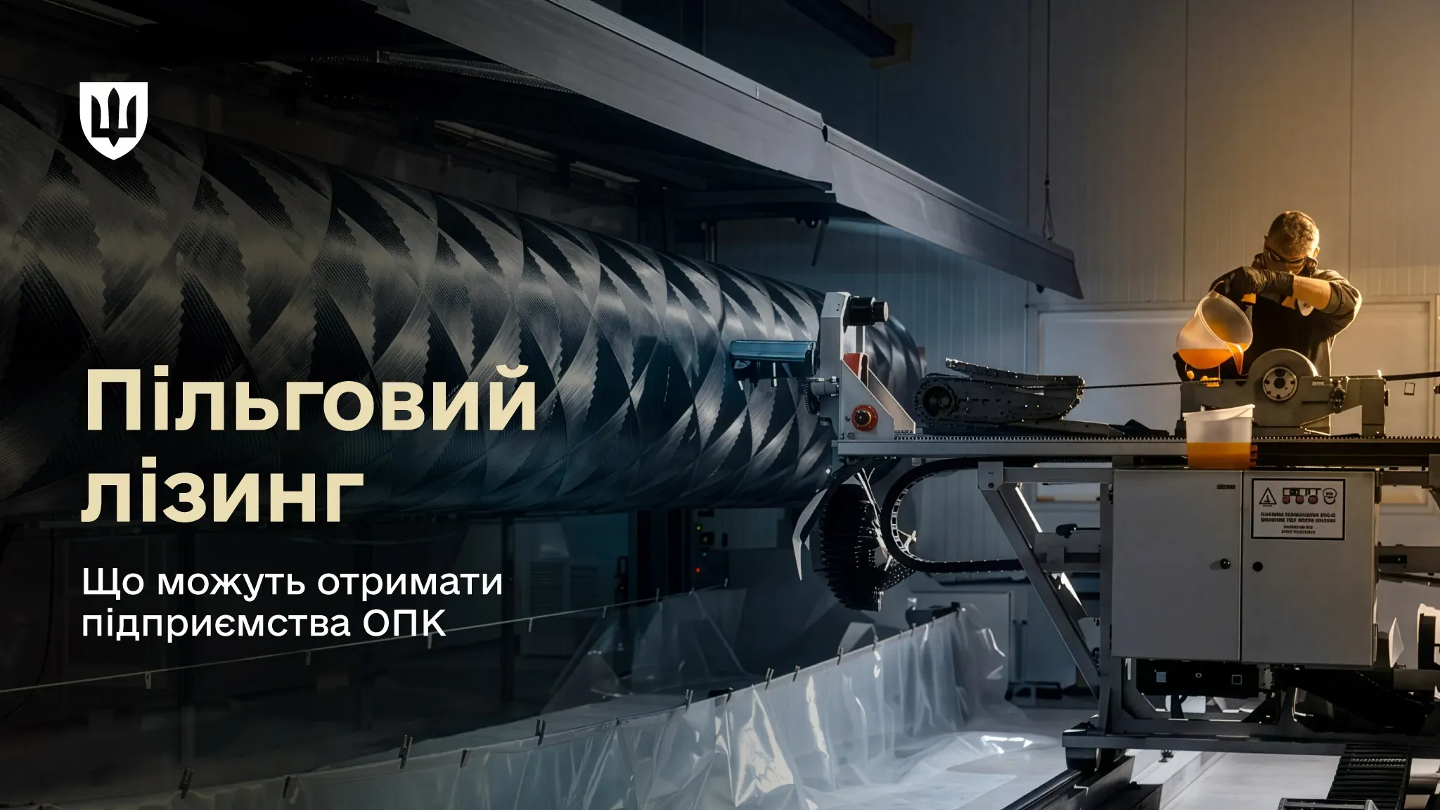 Працівник працює біля промислового обладнання на виробництві, наливаючи рідину поруч із великою циліндричною деталлю з вуглеволокна