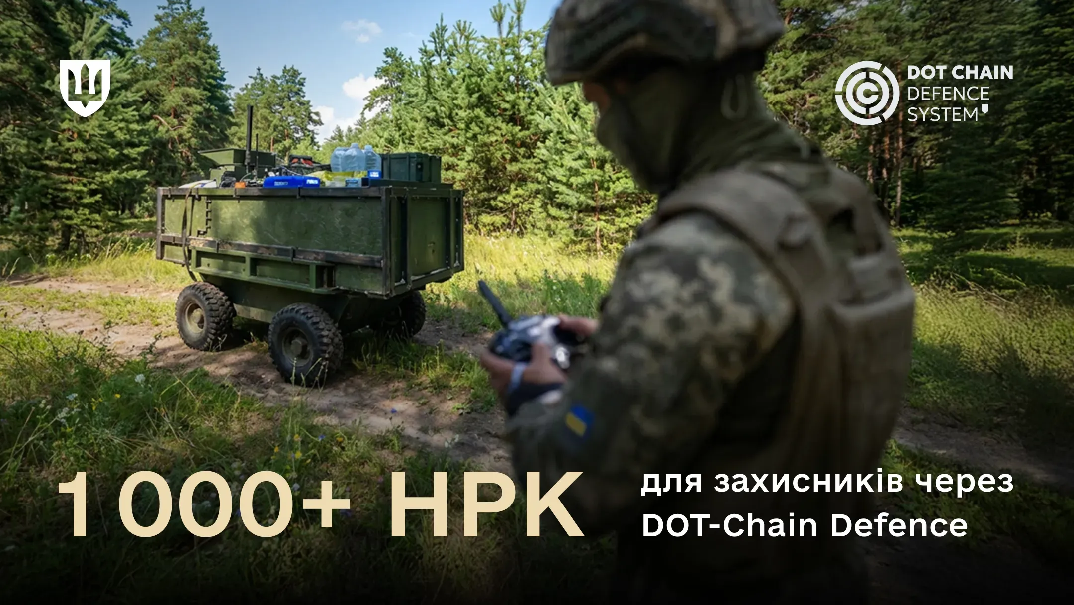 Колісний НРК завантажений ящиками та бутлями з водою, стоїть на лісовій дорозі. Праворуч від нього український військовий  керує платформою за допомогою дистанційного пульта