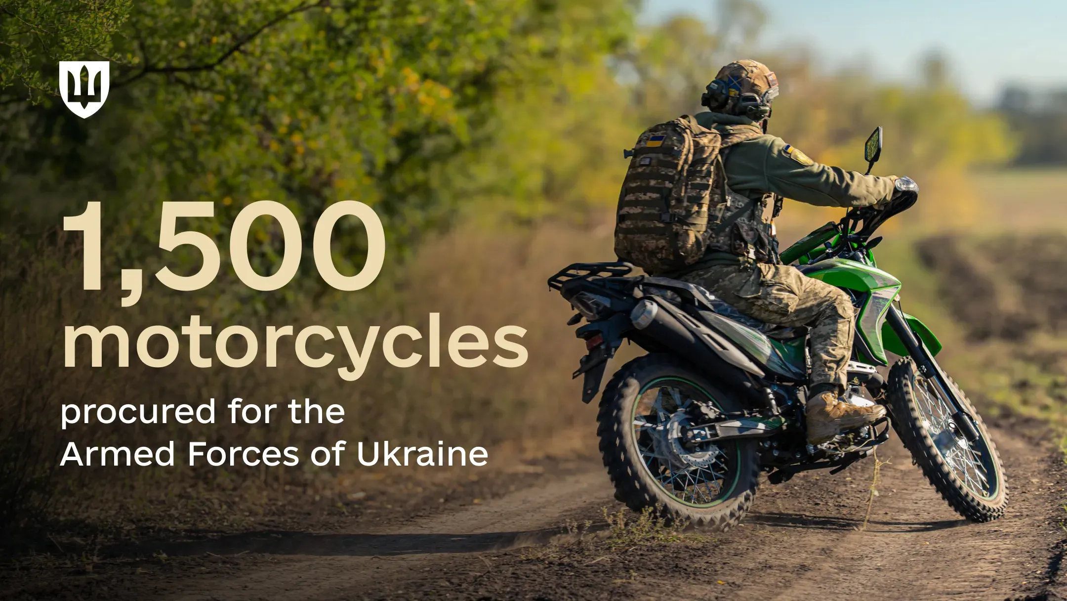A service member in military gear rides a green motorcycle along a dirt road