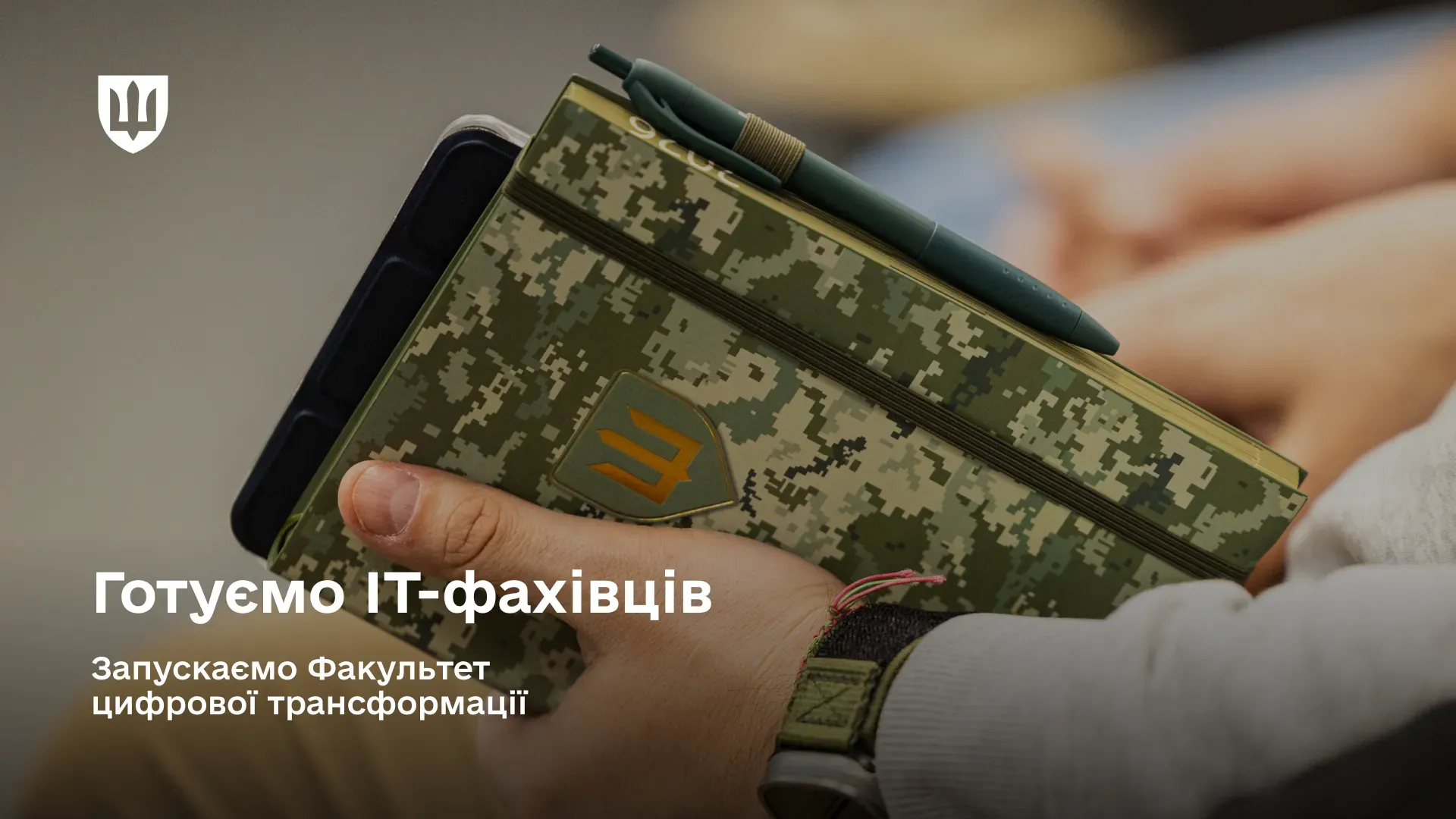 Рука тримає блокнот у військовому камуфляжі з ручкою; на зображенні напис: «Готуємо ІТ-фахівців. Запускаємо факультет цифрової трансформації»