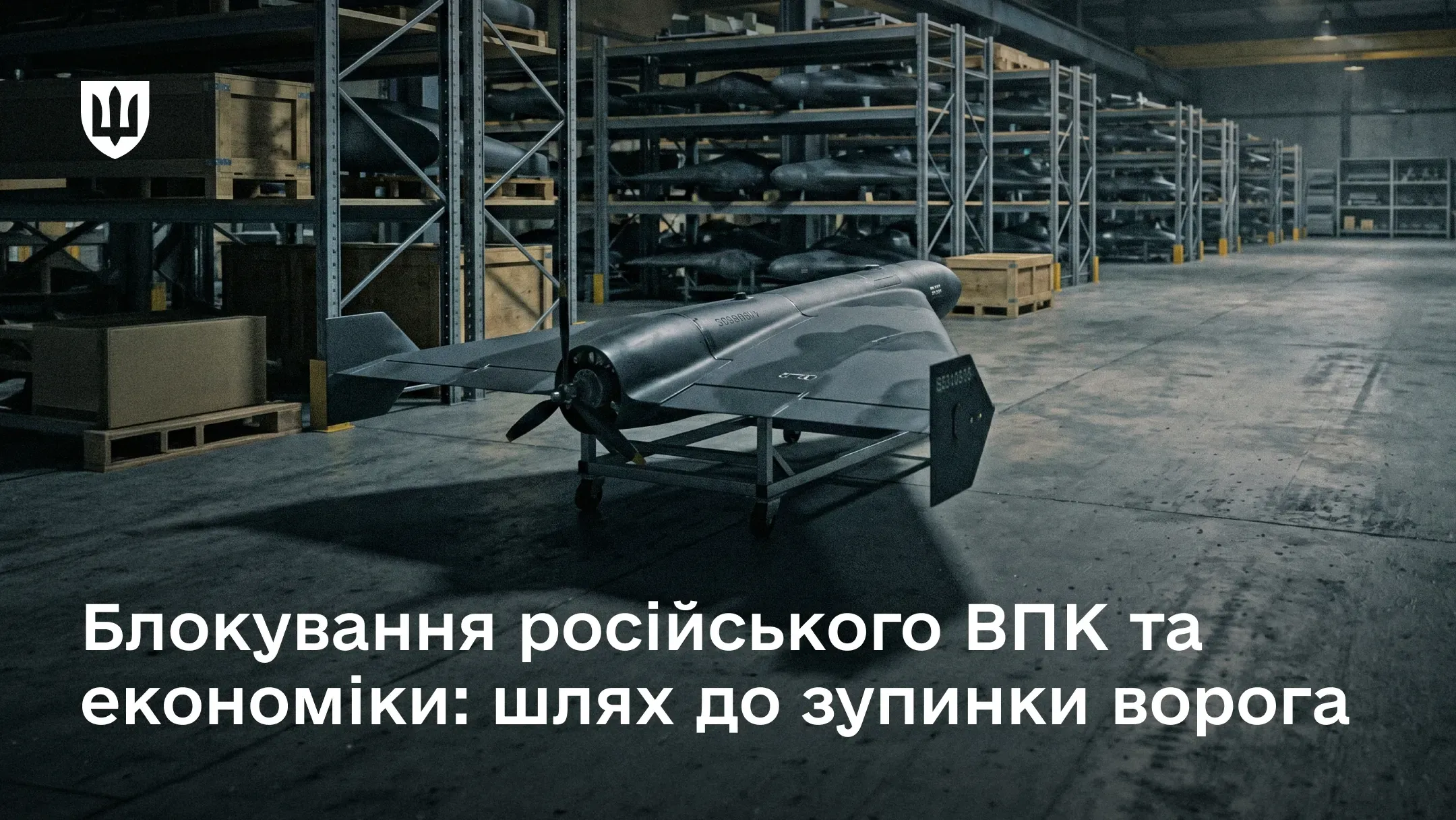 Темний ударний безпілотник на підставці посеред великого складського приміщення, заповненого стелажами.