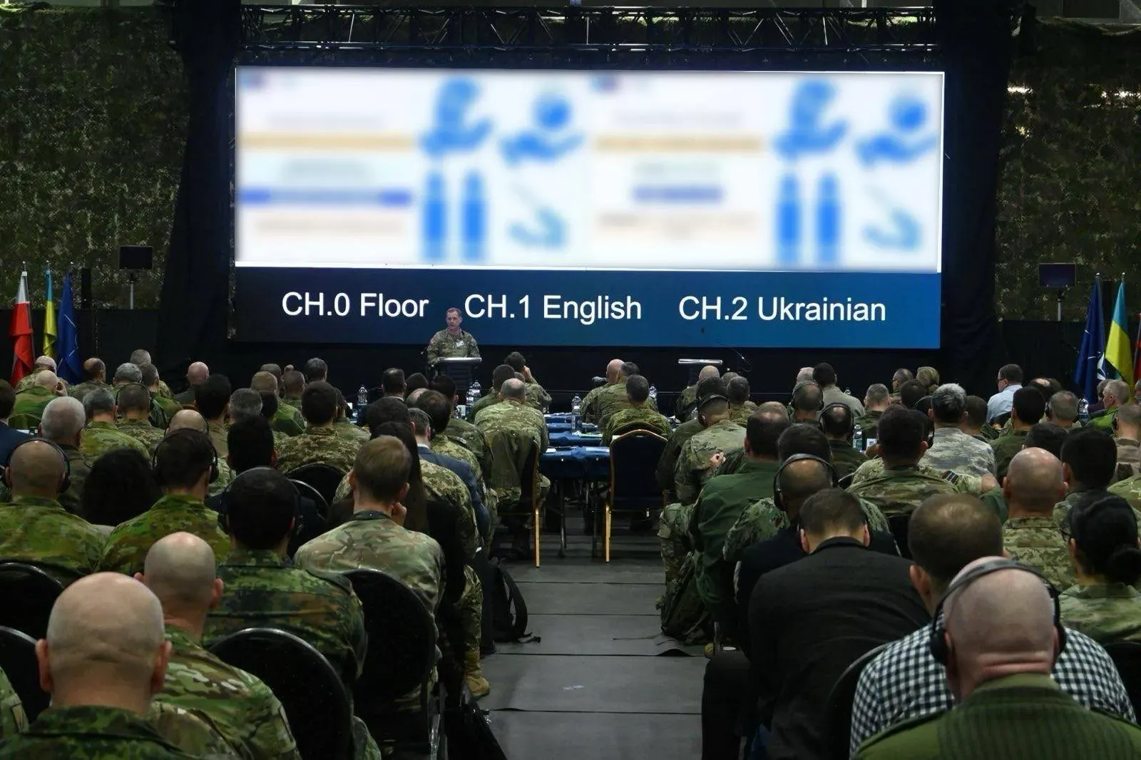Вид із задньої частини зали на конференцію OFDEF. Велика кількість військових у камуфляжній формі слухають доповідача, який стоїть перед великим екраном