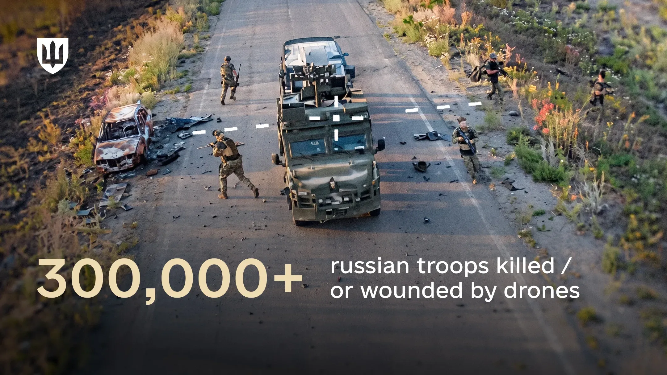 A view through a sight showing a road with a military vehicle and armed personnel next to a burned-out car. Text on the image: 300,000+ russian troops killed or wounded by drones
