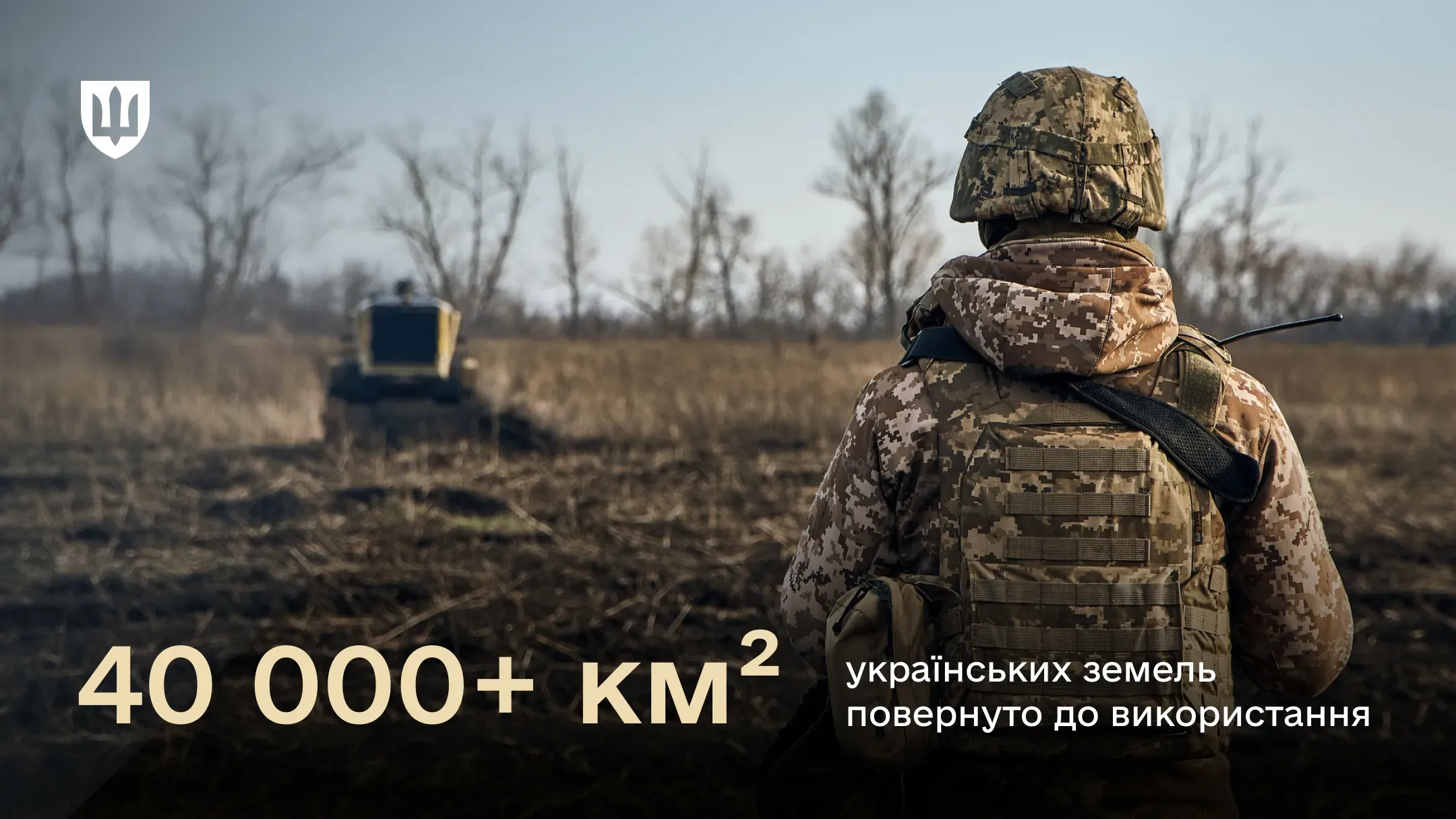 Фото українського військового зі спини, який дивиться на поле, де працює   техніка з розмінування