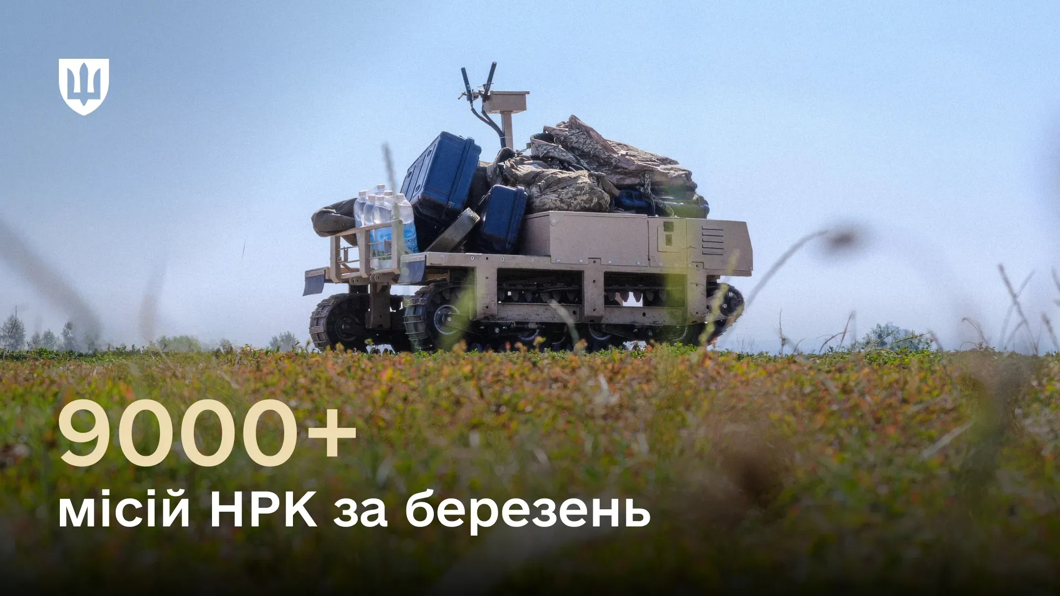 Наземний роботизований комплекс на гусеничному ходу рухається через поле, завантажений військовим спорядженням, ящиками та пляшками з водою