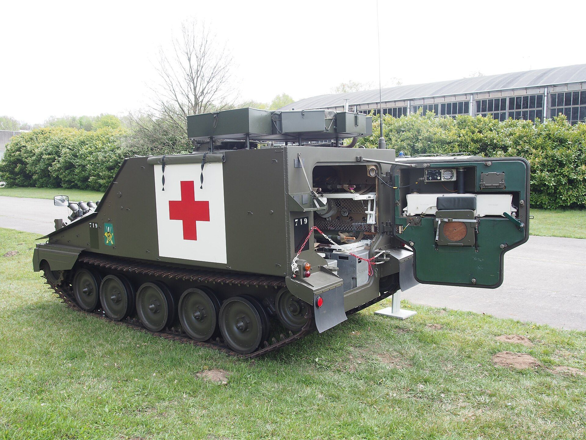 Dark green tracked armoured ambulance with a large red cross on a white panel on the side. The rear doors are open, revealing the medical equipment within