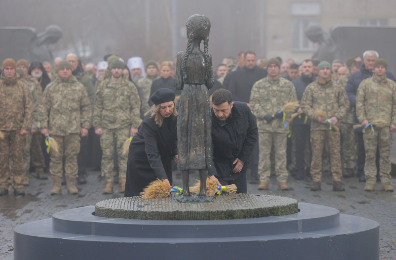 President Volodymyr Zelenskyy and First Lady Olena Zelenska place symbolic wheat-ear tributes at the “Bitter Memory of Childhood” monument at the National Museum of the Holodomor-Genocide in Kyiv, with service members and government officials visible in the background