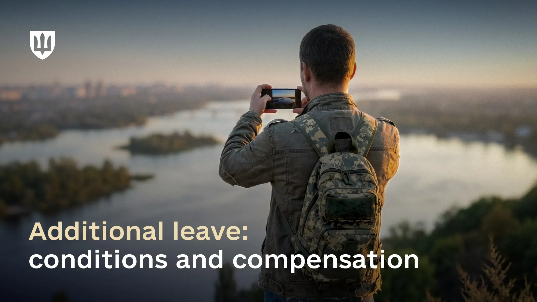 A man wearing an olive jacket and a camouflage backpack stands on elevated ground with his back to the camera