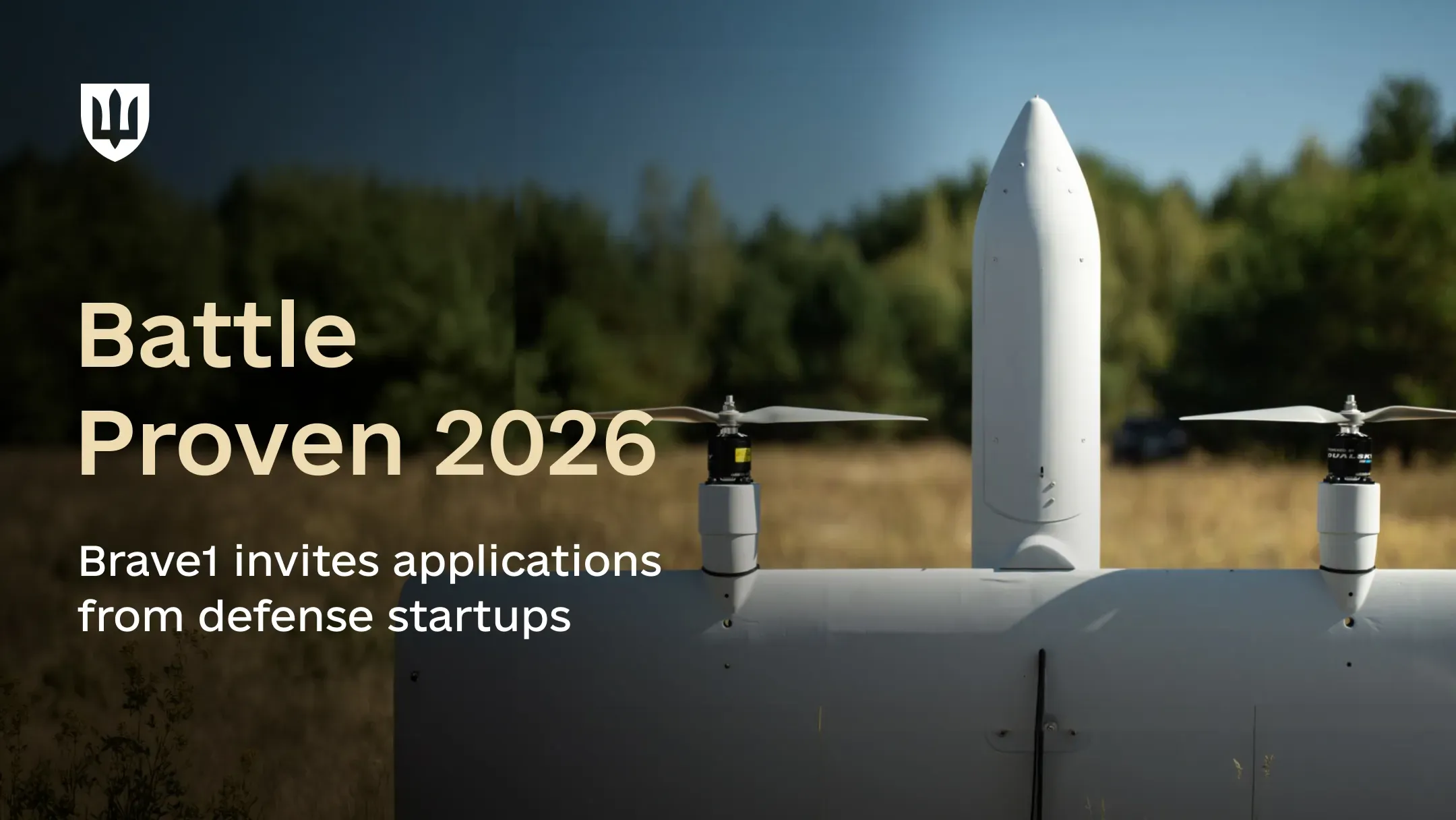 A white unmanned aerial vehicle (UAV) is positioned in a field against a forest backdrop. The image illustrates the announcement of the Battle Proven 2026 defense-tech startup competition.