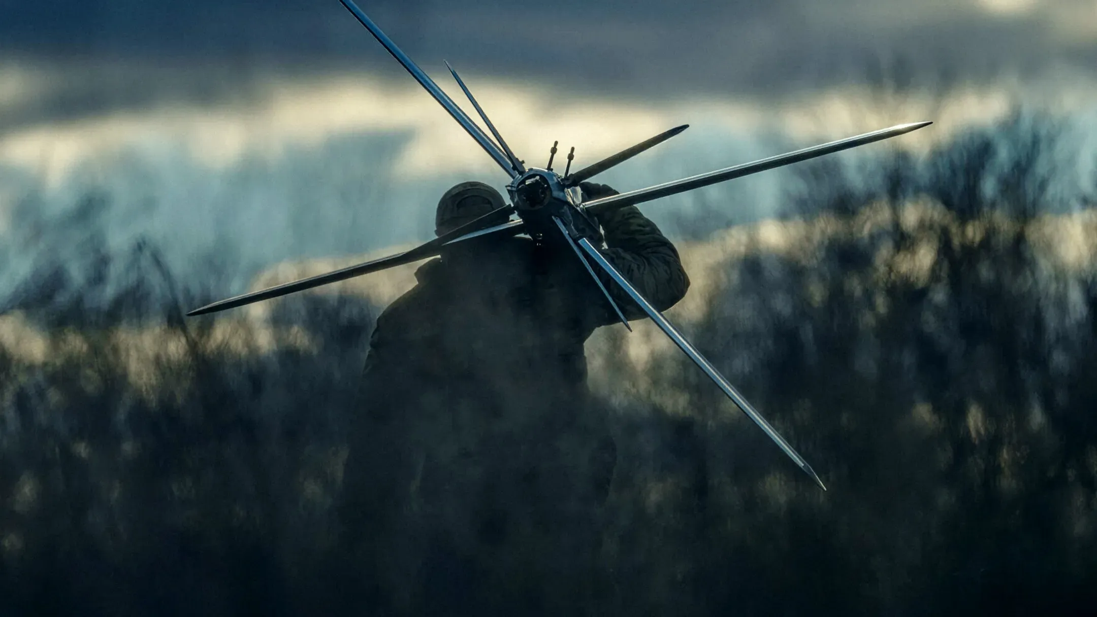 A Ukrainian service member holding a mid-strike drone, with a forest in the background