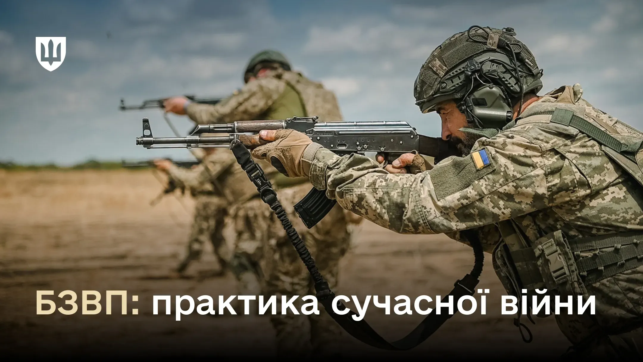 Український військовий у камуфляжі, тактичних навушниках та рукавичках, з українським прапором на нашивці, прицілюється з автомата АК на піщаному полігоні.