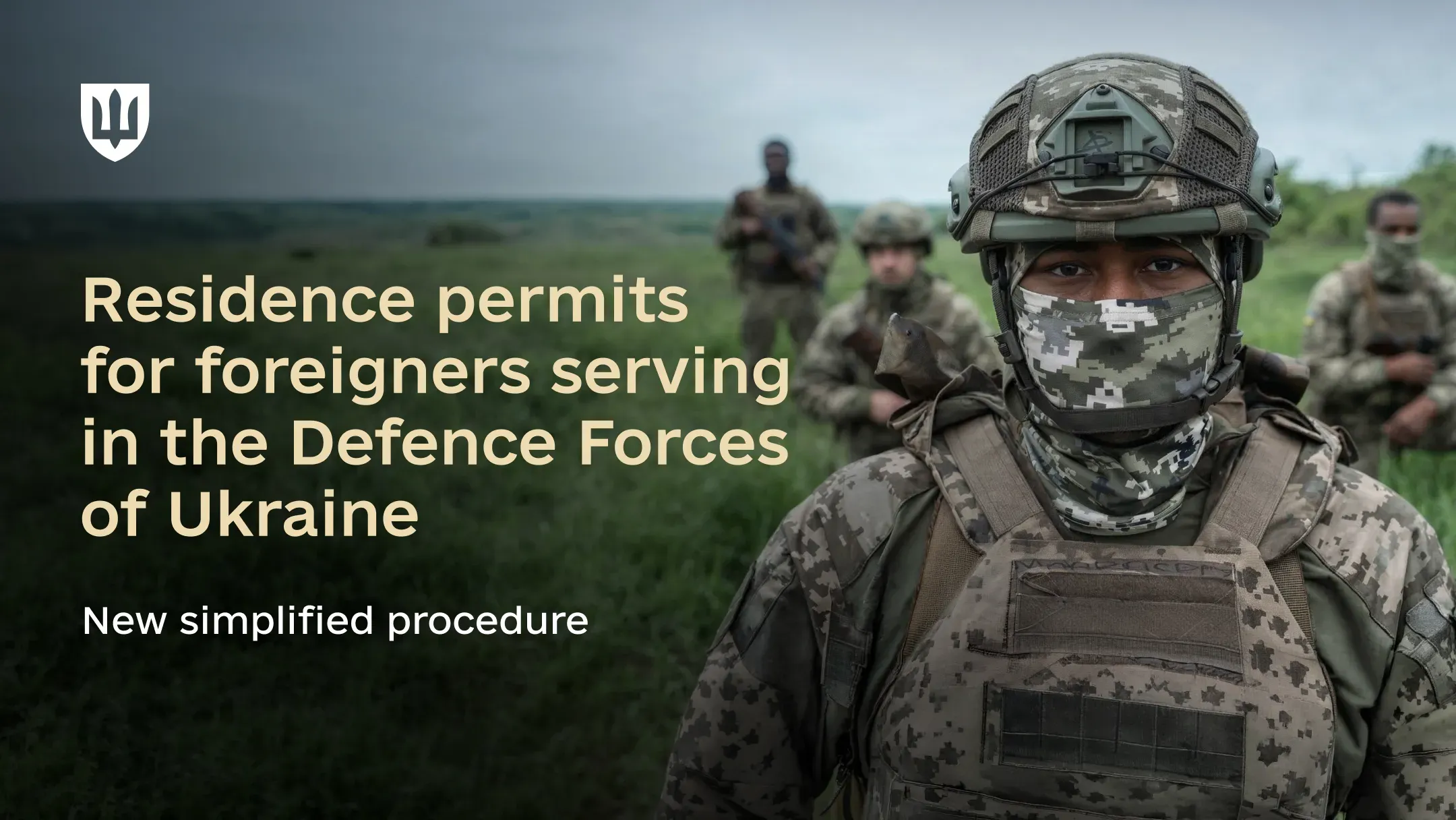A service member in uniform in the foreground, with other service members on open terrain in the background.