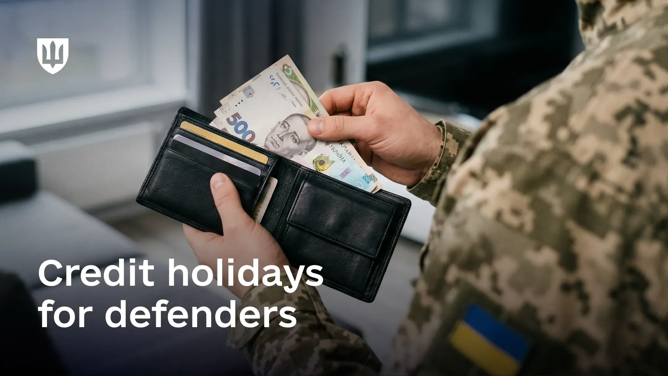 "A service member in a camouflage-pattern uniform holds an open black wallet with Ukrainian 500-hryvnia banknotes visible inside. At the bottom, large white text reads: “Credit holidays for defenders”."