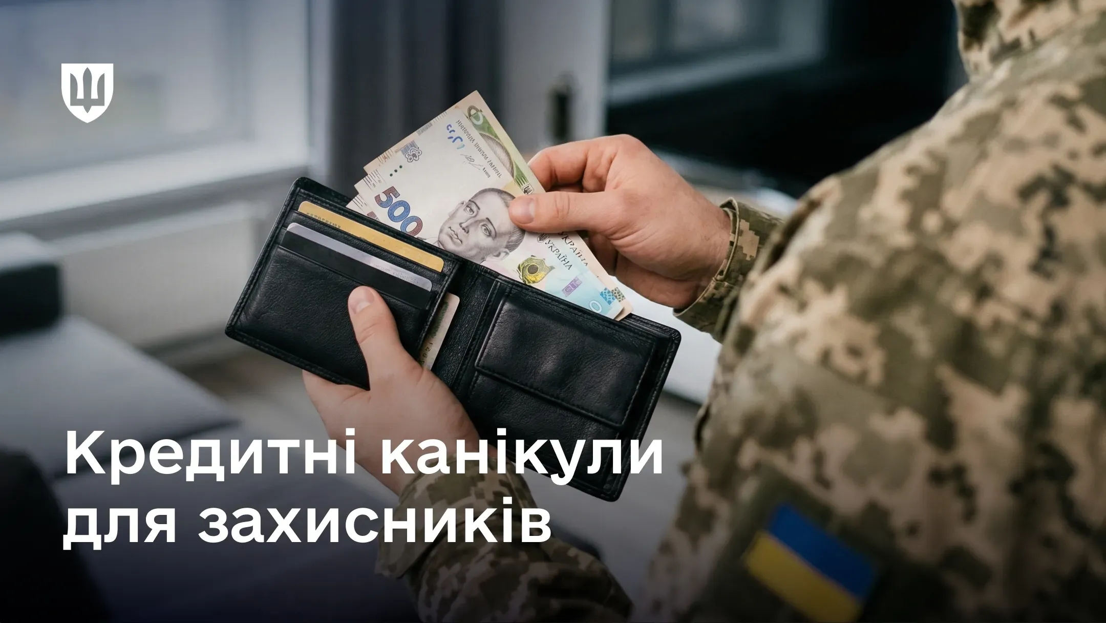Військовий у камуфляжі тримає відкритий чорний гаманець із купюрами української гривні номіналом 500 гривень. Внизу великий білий текст: «Кредитні канікули для захисників»