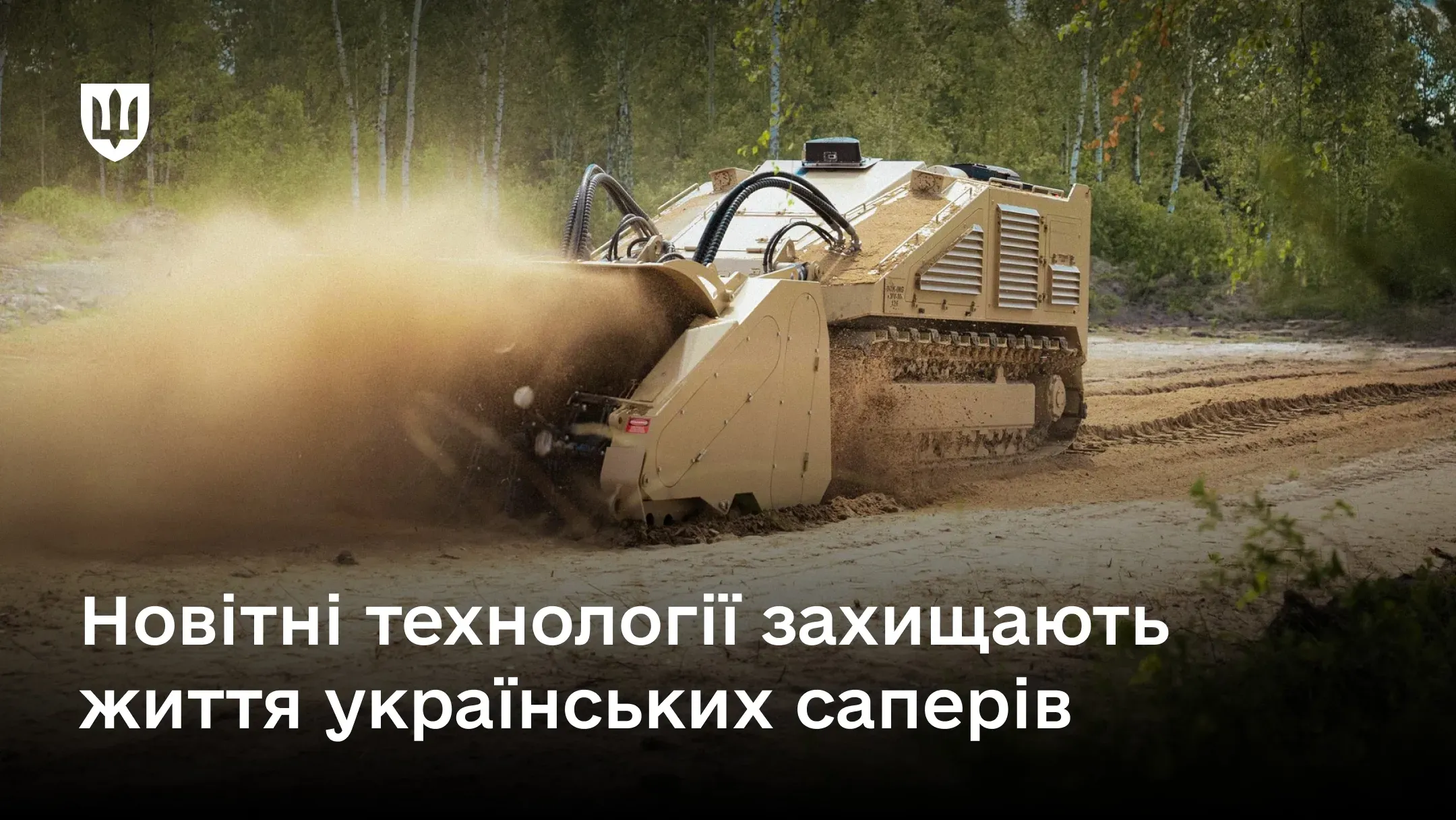 Гусенична безпілотна машина для розмінування бежевого кольору рухається піщаною ділянкою місцевості вздовж лісосмуги, піднімаючи попереду себе велику хмару пилу та піску