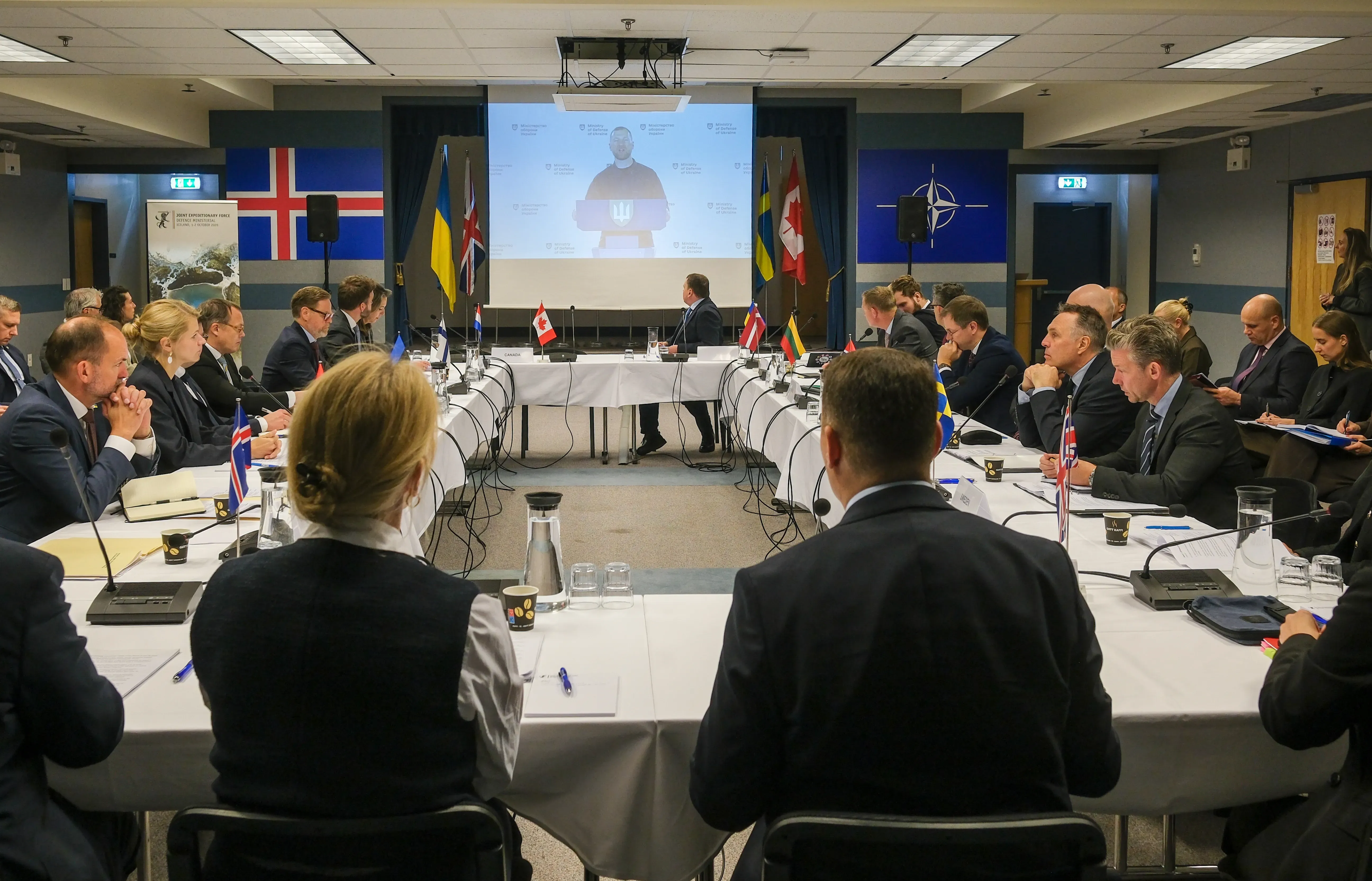 JEF meeting participants sit at tables during a video link with Evgeniy Khmara