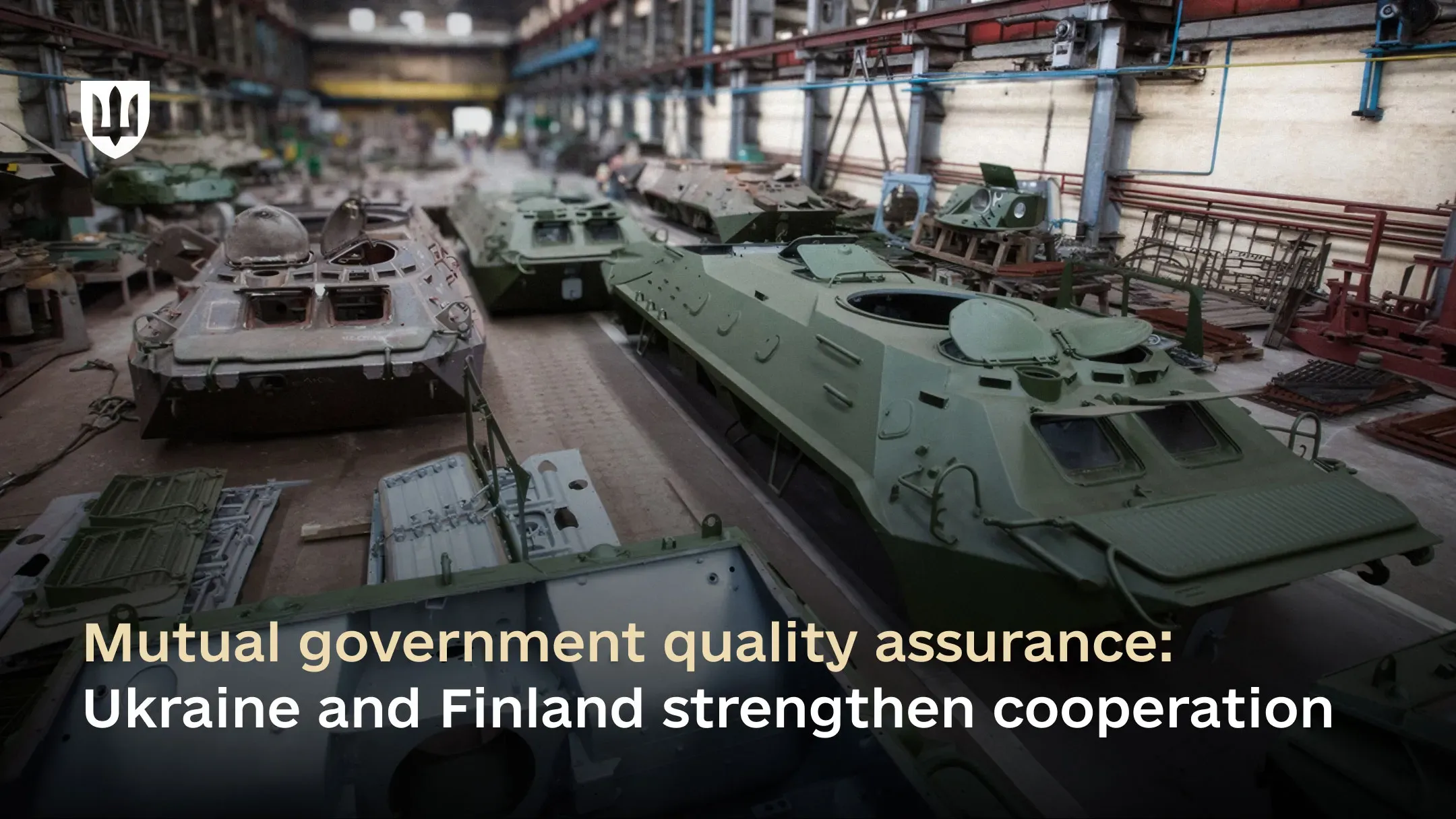 A defence industry workshop with armoured vehicles at various stages of repair. The Ukrainian coat of arms appears at the top, and at the bottom, the overlaid text reads: “Mutual government quality assurance: Ukraine and Finland strengthen cooperation.”