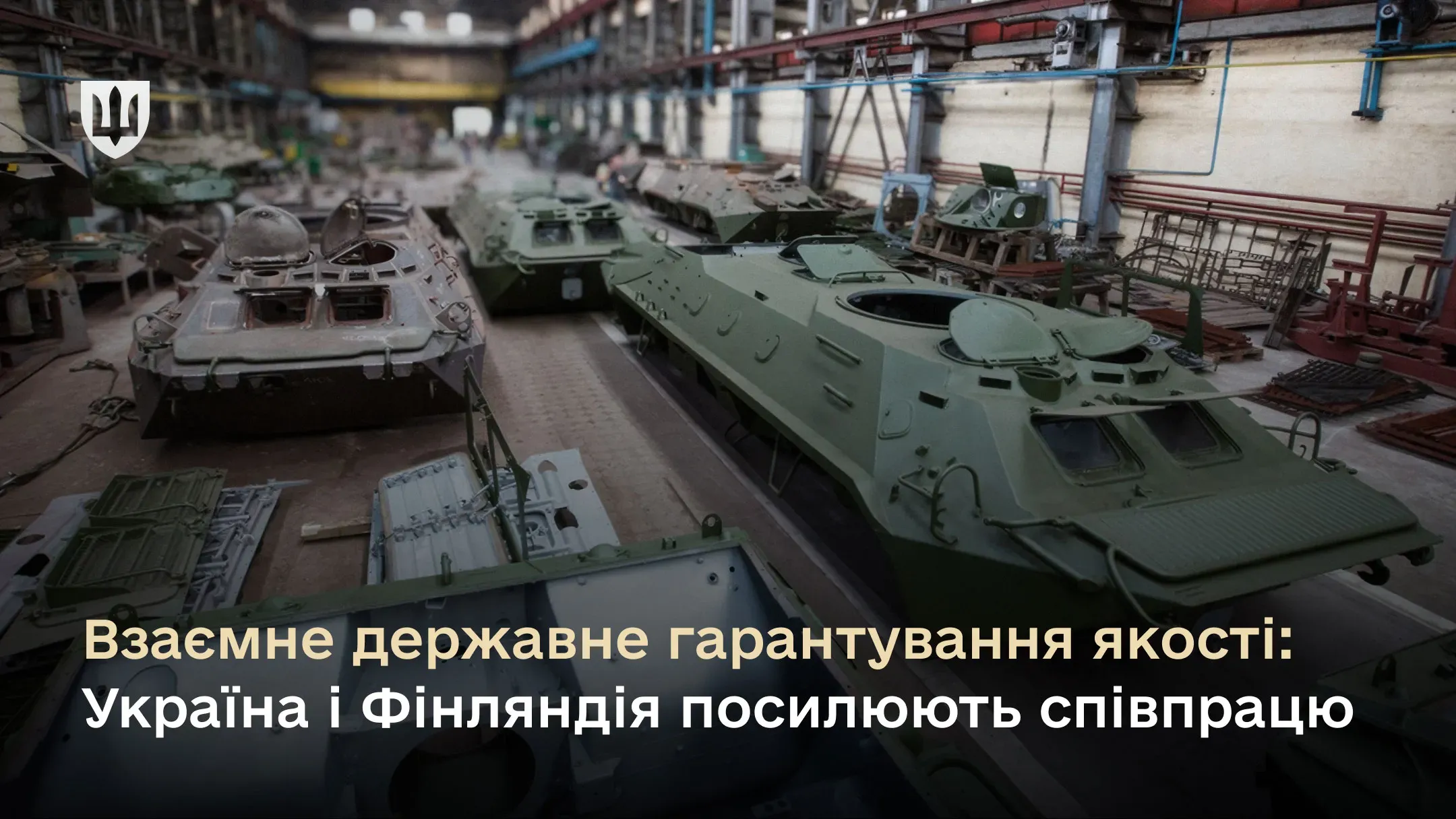 На фото цех оборонного підприємства з бронетехнікою на різних етапах ремонту. Зверху герб України, знизу напис про посилення співпраці України та Фінляндії у сфері державного гарантування якості.