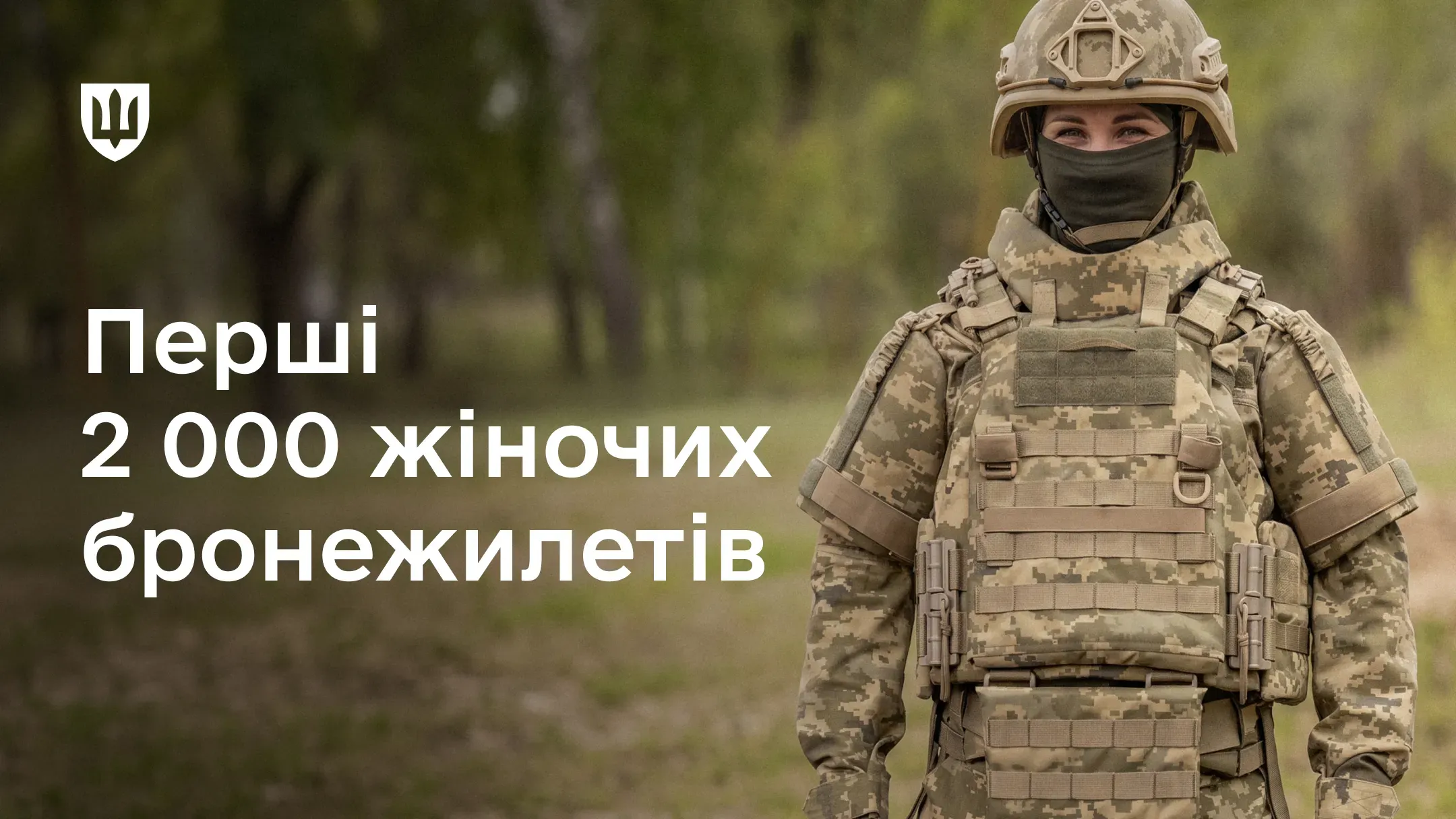 Українська військовослужбовиця у повному екіпіруванні та спеціальному бронежилеті стоїть на тлі дерев