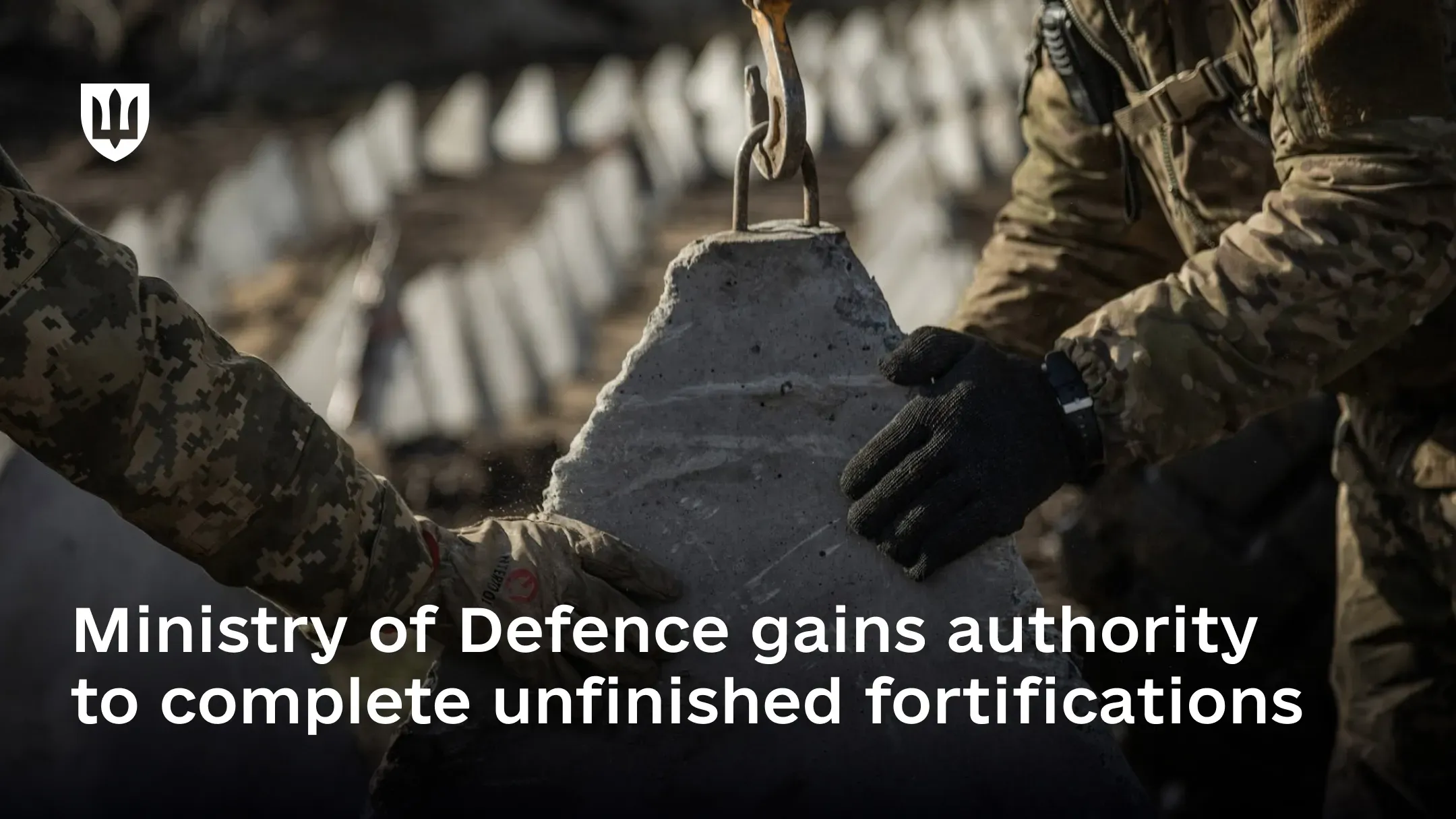 Ukrainian service members install a concrete fortification structure, with overlaid text about the Ministry of Defence being authorized to complete unfinished fortifications