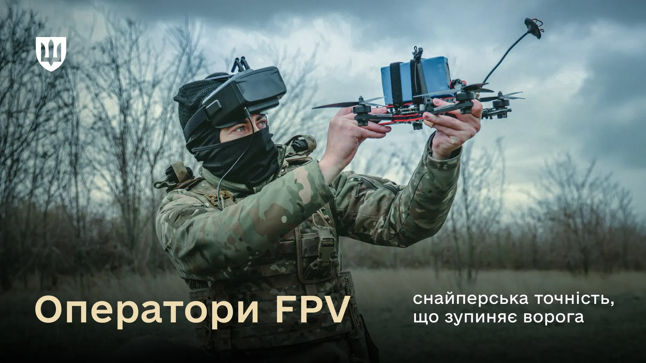 Військовий у повному тактичному екіпіруванні, камуфляжі мультикам, тактичній масці та FPV-окулярах тримає перед собою квадрокоптер FPV, готуючись до запуску