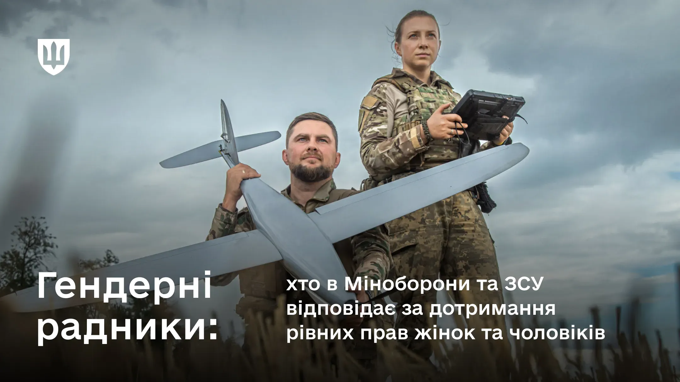 На фоні хмарного неба сидить чоловік у військовій формі тримає БПЛА, у нього за спиною стоїть жінка з пультом керування