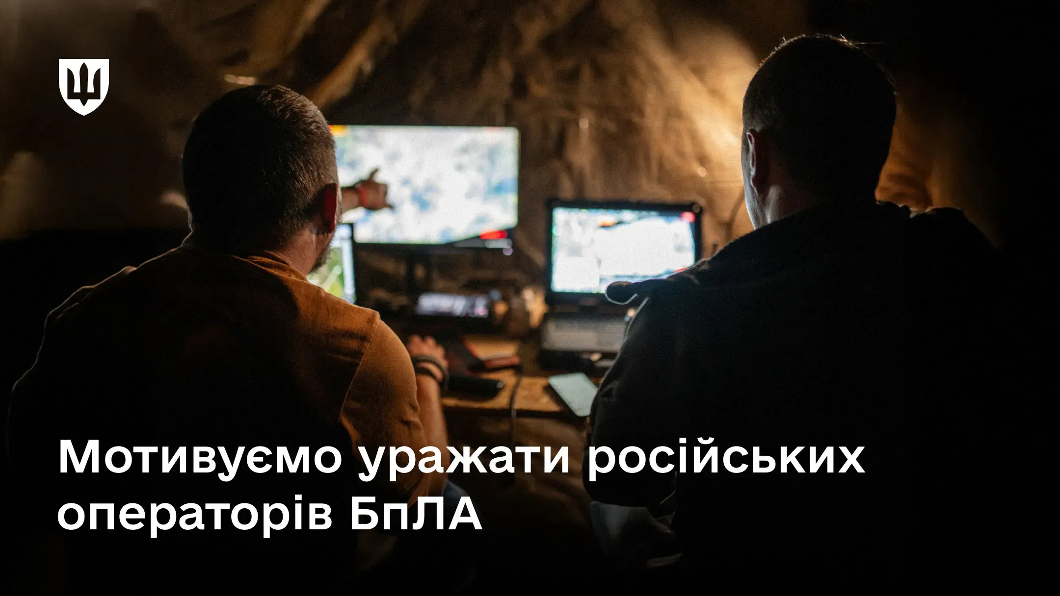 Двоє військовослужбовців сидять у темному бліндажі перед увімкненими моніторами та ноутбуком