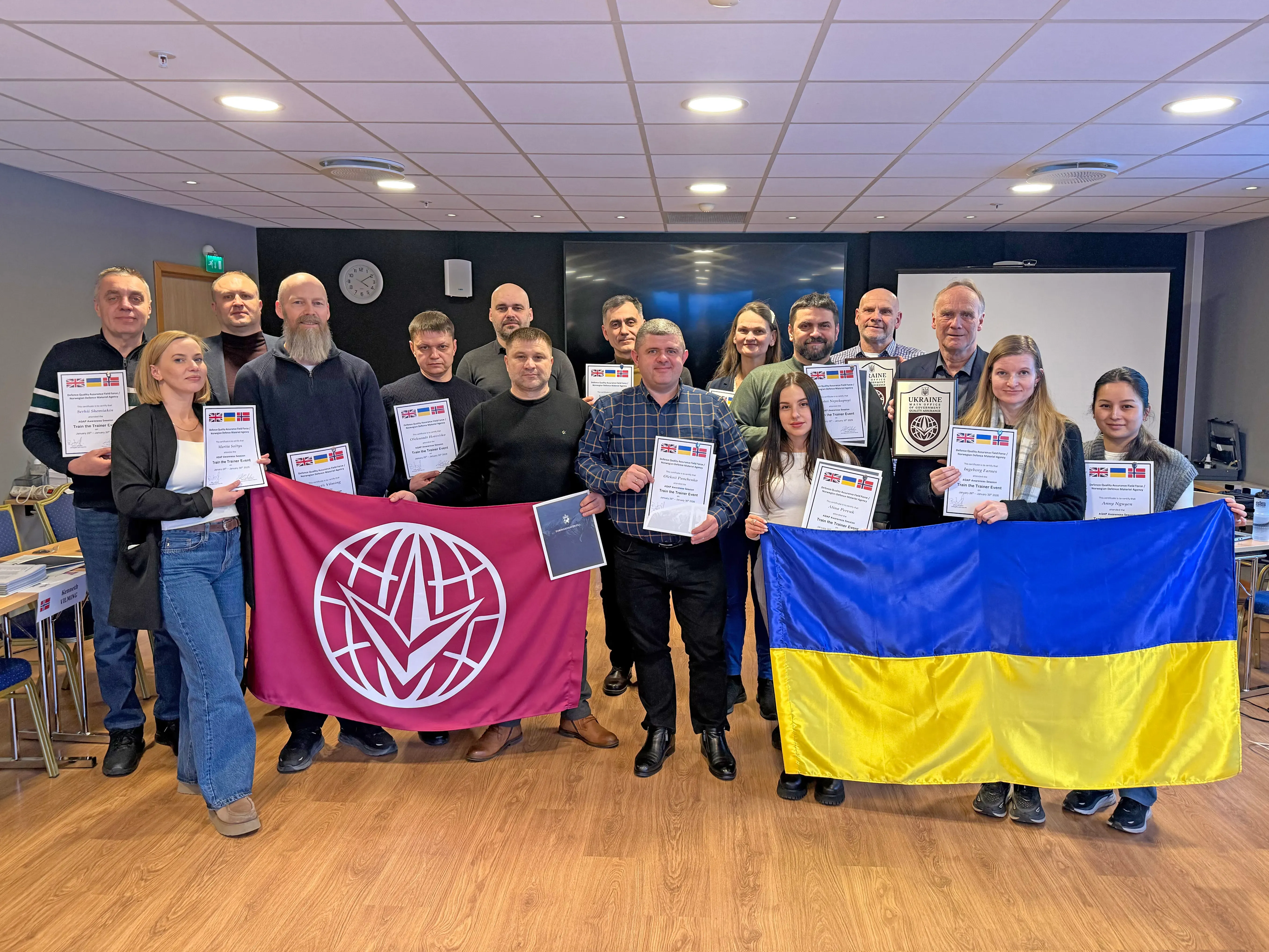 A group of participants pose in a training room holding certificates, the Ukrainian flag, and a conformity mark flag.
