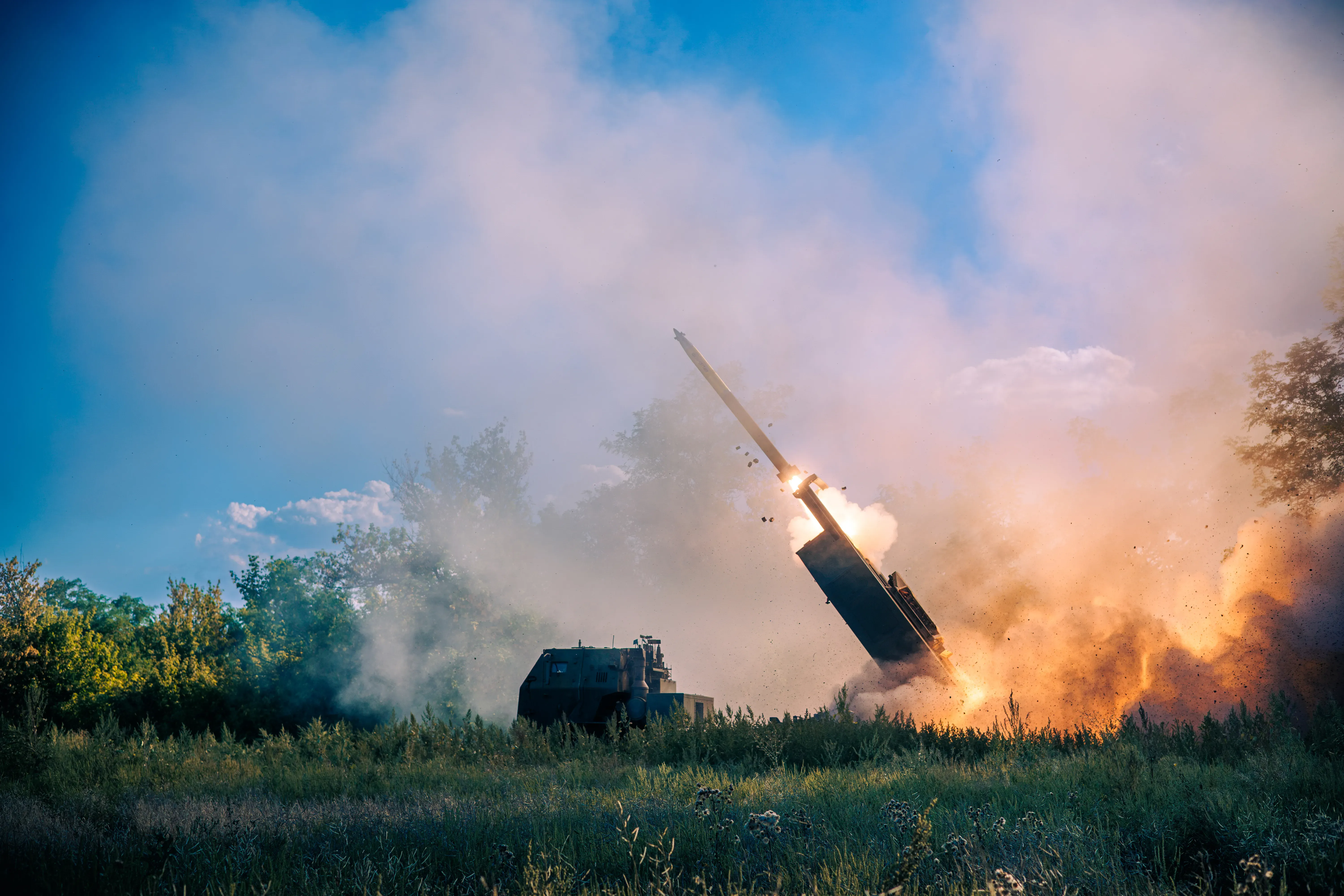 Пусковий модуль M142 HIMARS у момент пуску ракети, навколо клуби диму й полум'я