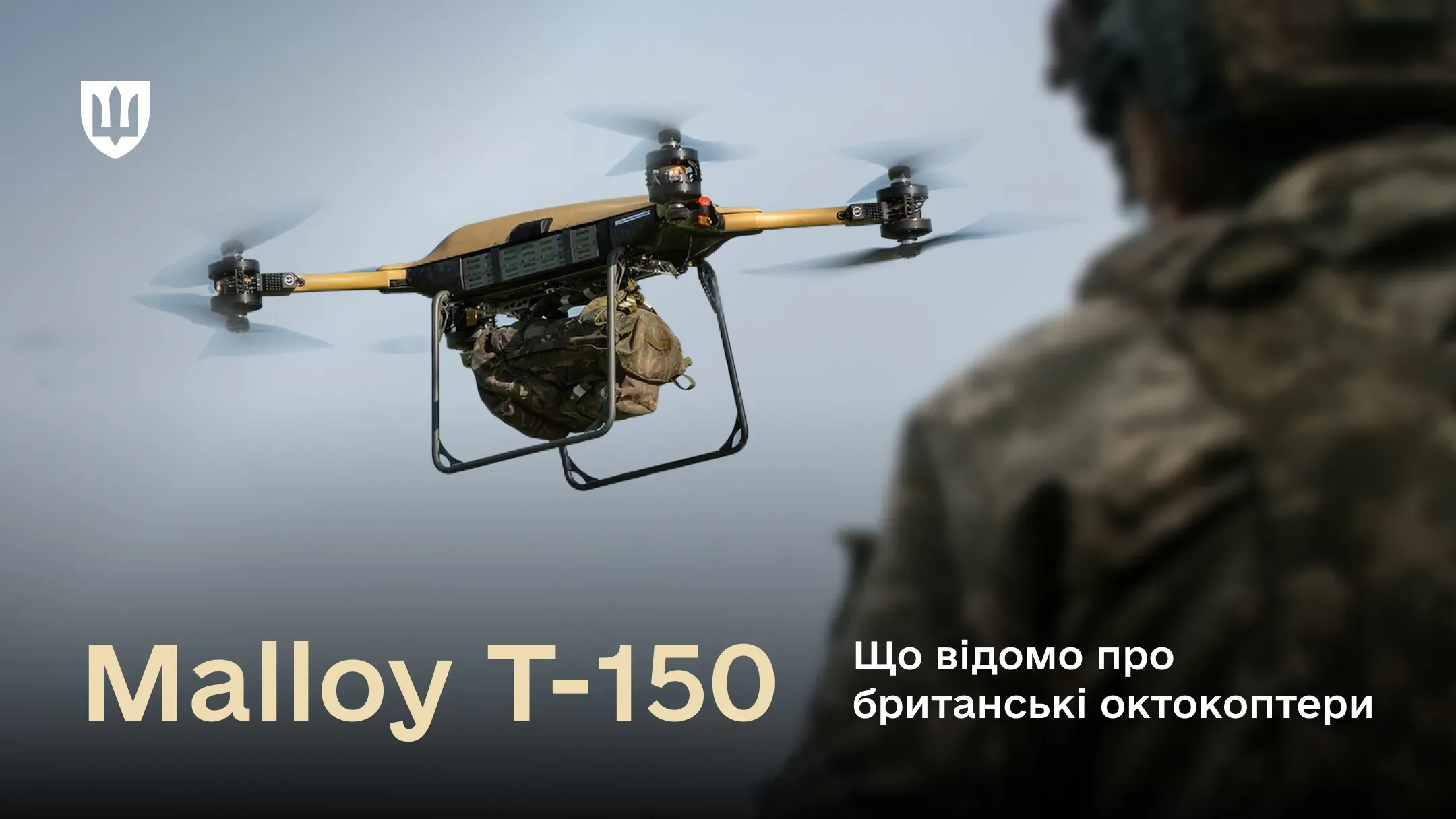 Військовий вантажний дрон Malloy T-150 у польоті на фоні туманного ландшафту. До його нижньої частини прикріплений великий тактичний рюкзак у камуфляжі. На передньому плані видно плече та голову військового у формі, який спостерігає за польотом