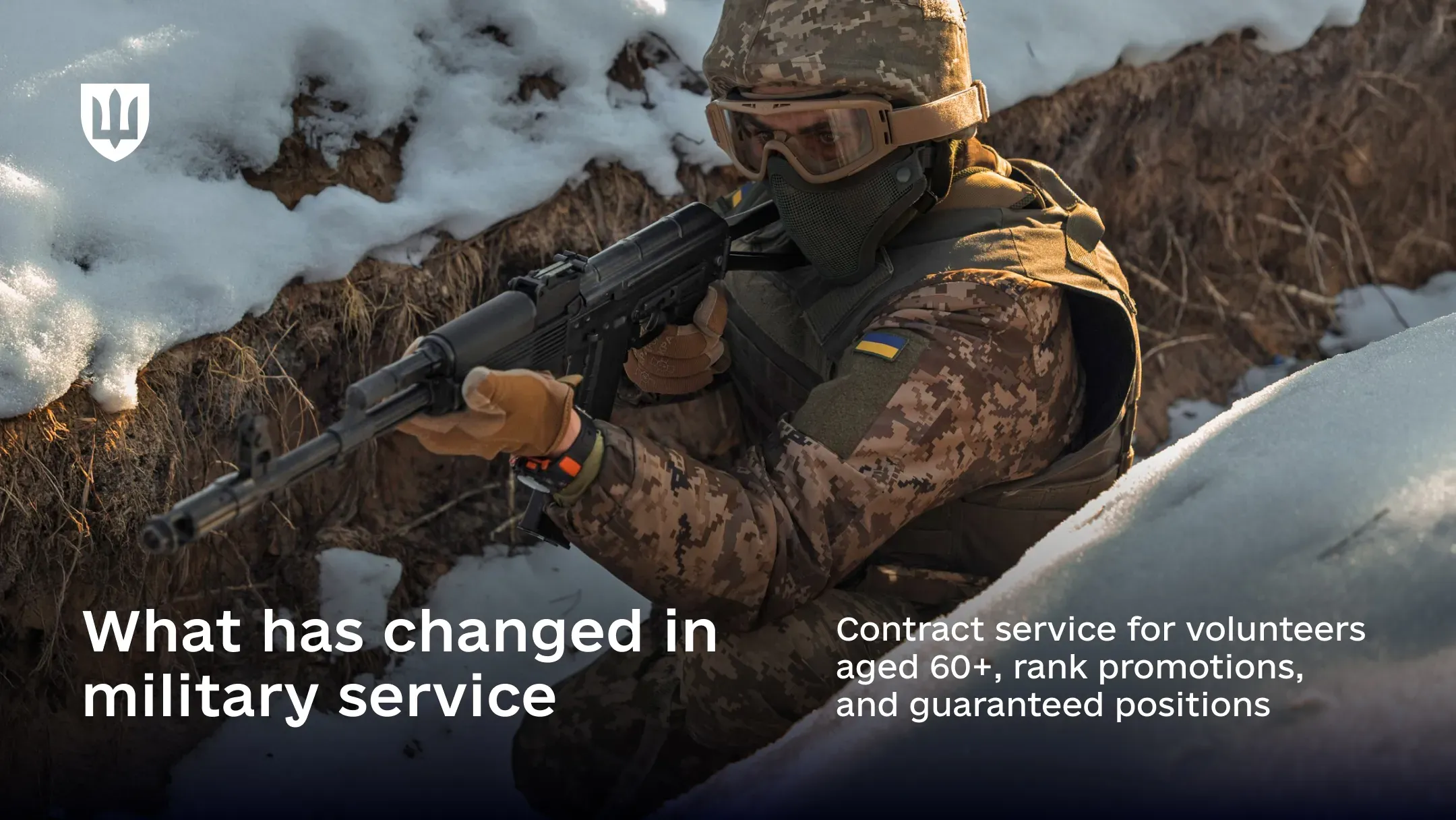 A Ukrainian service member in full combat gear holds a rifle while positioned in a snow-covered trench