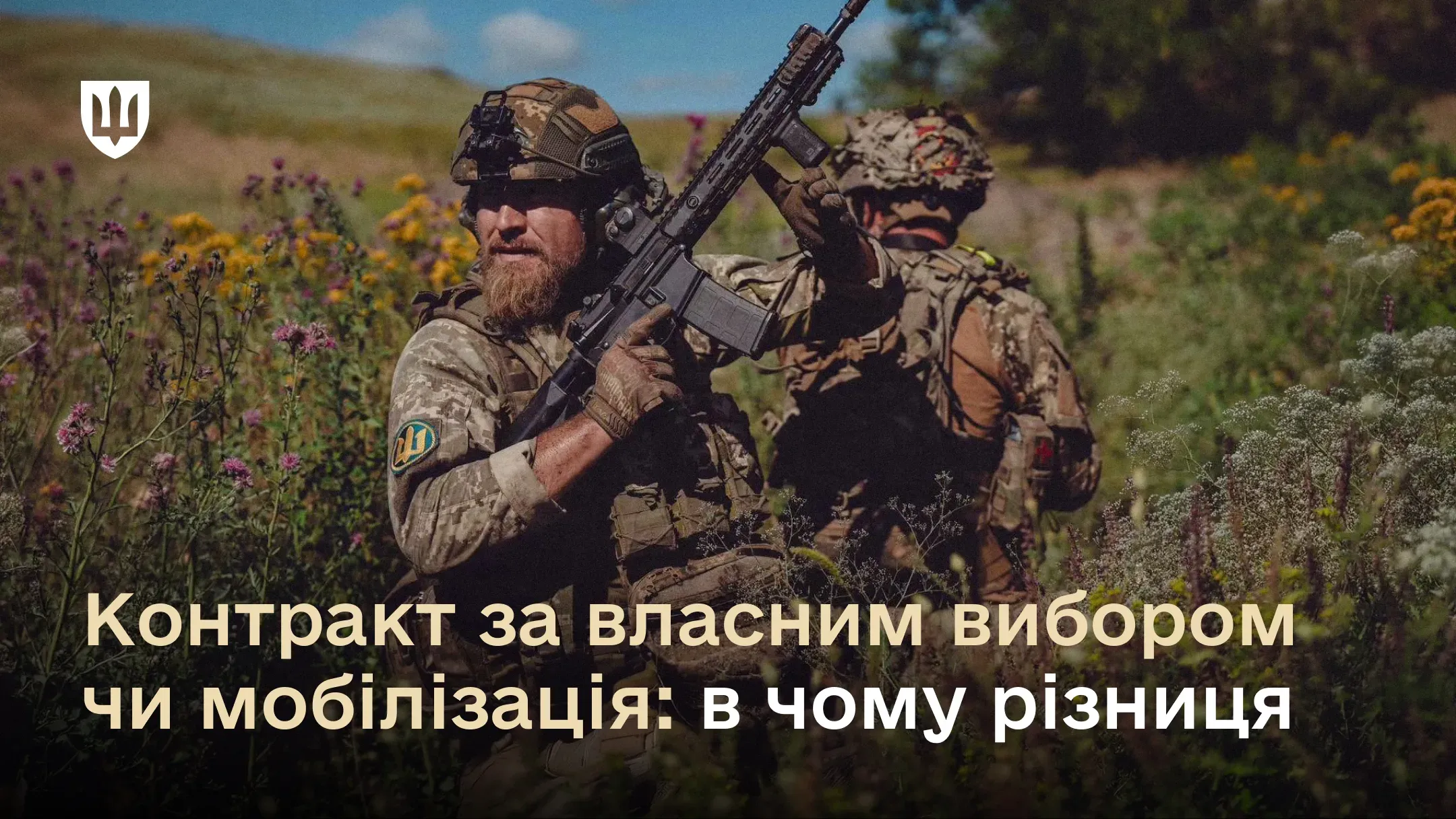 Двоє військовослужбовців у камуфляжній формі та екіпіруванні знаходяться серед поля влітку. На передньому плані — боєць із бородою, який тримає в руках штурмову гвинтівку