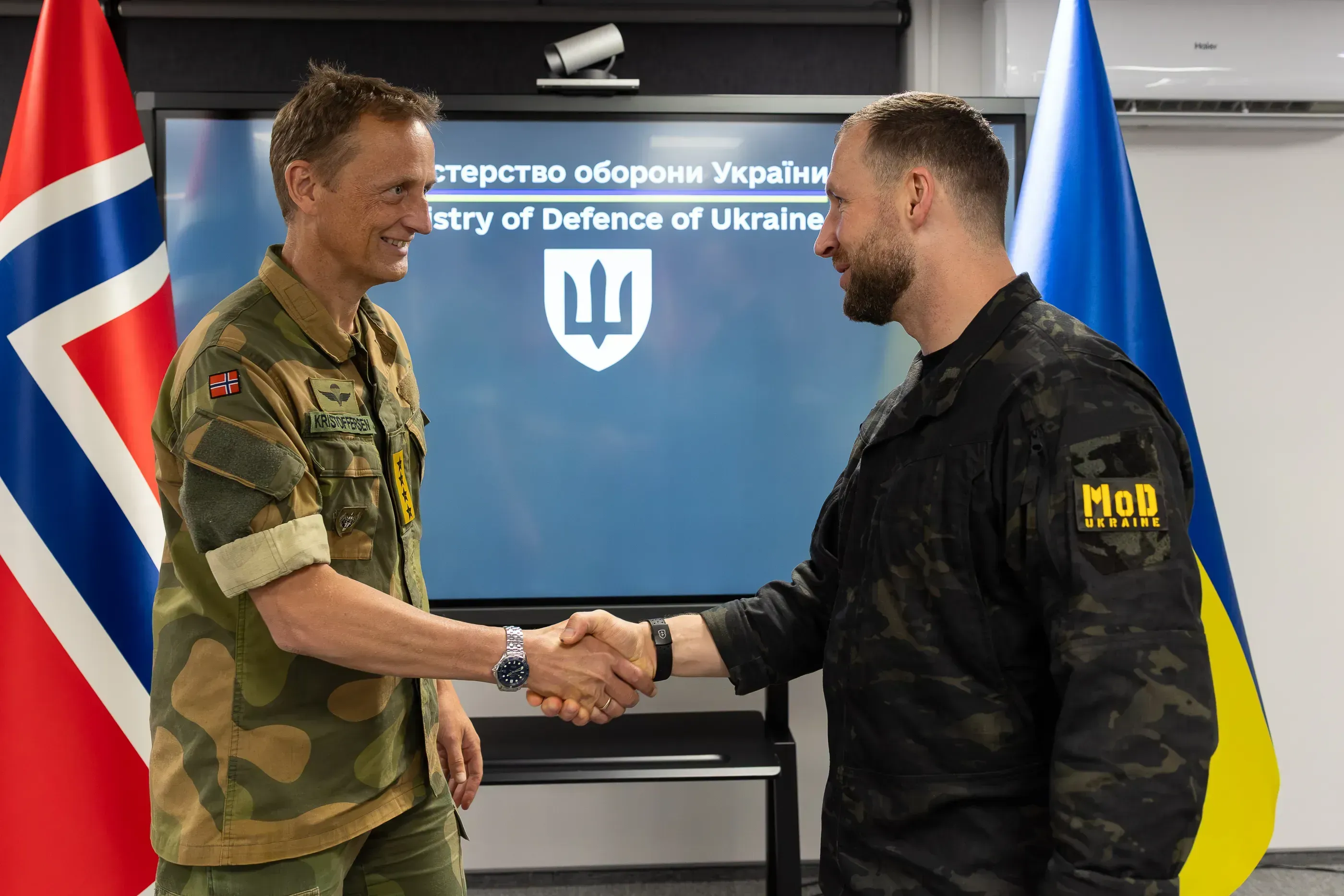 Evgeniy Khmara and Eirik Kristoffersen shaking hands against a backdrop of Ukrainian and Norwegian flags and a screen with the Ministry of Defence emblem