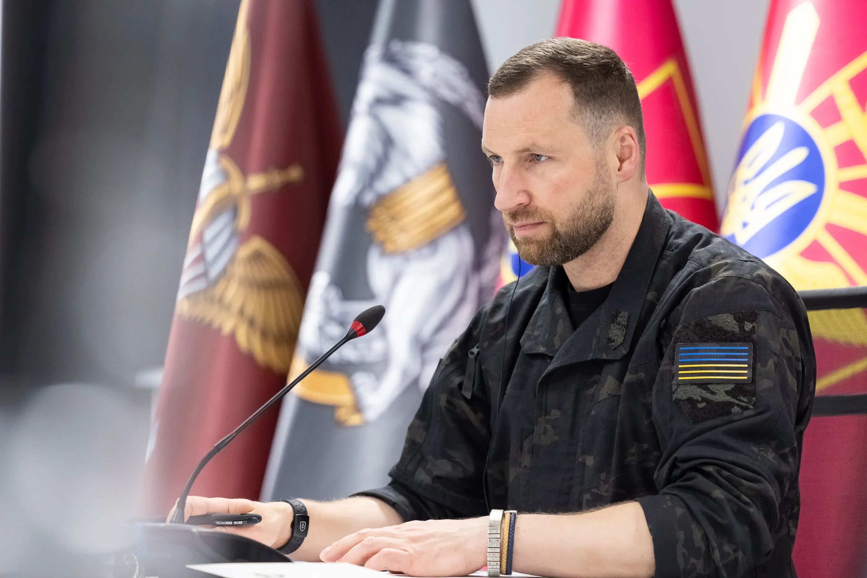 Євгеній Хмара за столом із мікрофоном на тлі офіційних прапорів