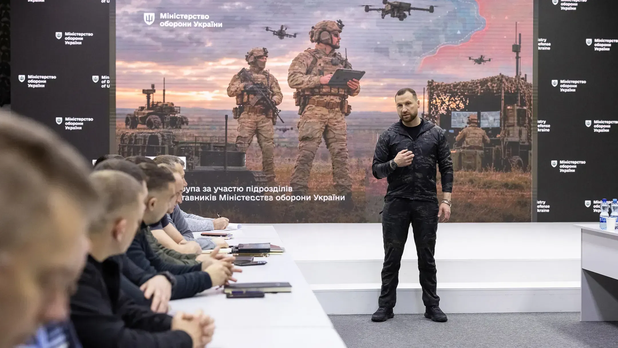 Minister of Defence of Ukraine Evgeniy Khmara meets service members to discuss frontline needs and effective command practices, with a battlefield display in the background