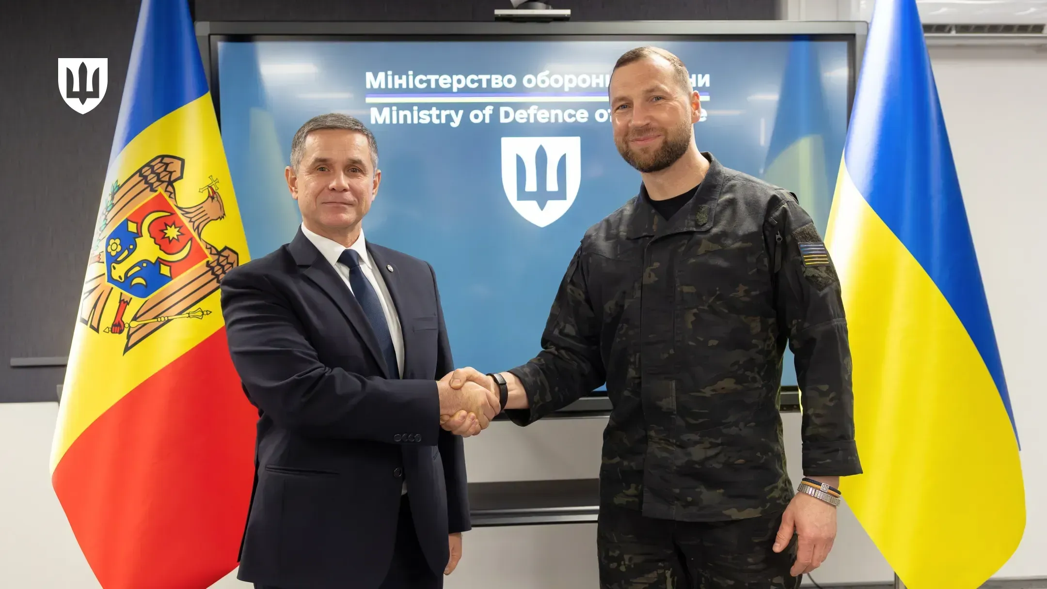 The defence ministers of Ukraine and Moldova shake hands after the meeting, with the flags of Moldova and Ukraine behind them