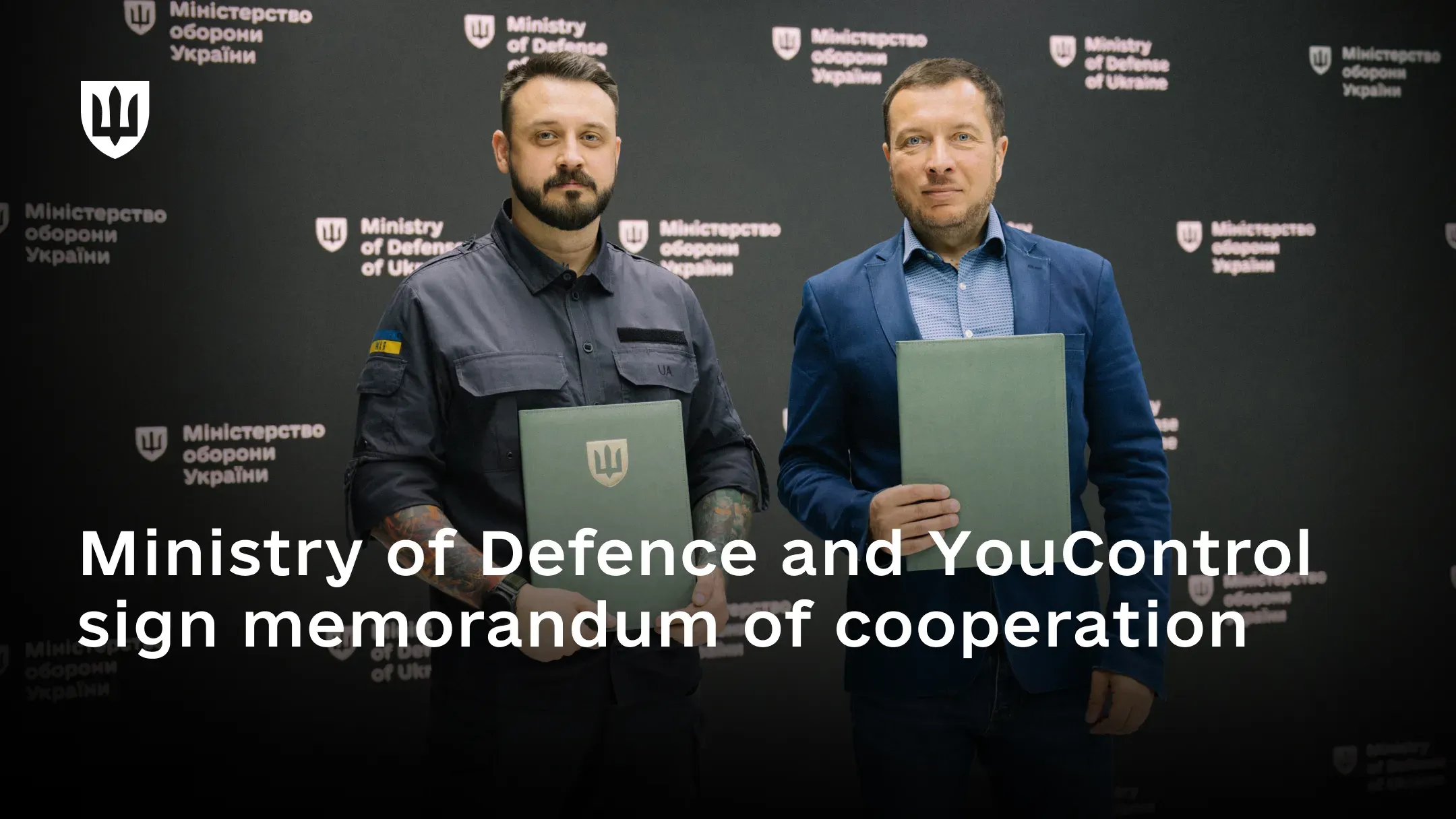 Mstyslav Banik and Danylo Hloba at the signing of the memorandum of cooperation between the Ministry of Defence and YouControl, standing side by side in front of a dark backdrop patterned with Ministry of Defence of Ukraine emblems