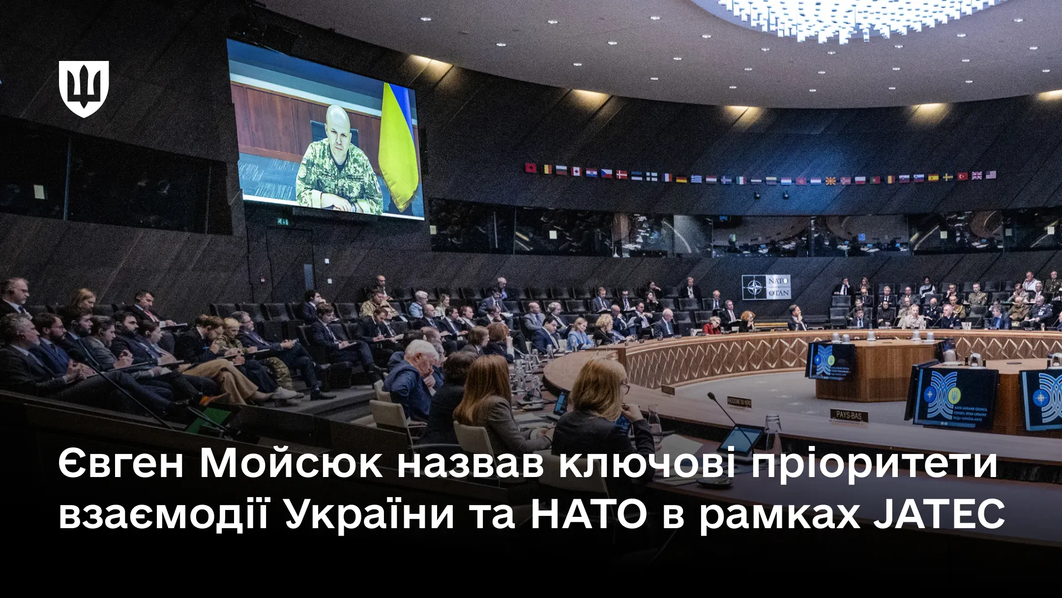 Велика конференц-зала круглої форми, в якій відбувається нарада. З великого екрану виступає заступник Міністра оборони України генерал-лейтенант Євген Мойсюк в піксельній формі
