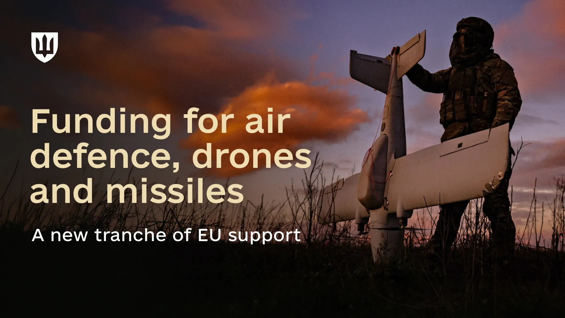 A serviceman in camouflage stands in a field at dusk holding a fixed-wing strike drone by the wing, against an orange and violet sky. Text reads: Funding for air defence, drones and missiles. A new tranche of EU support