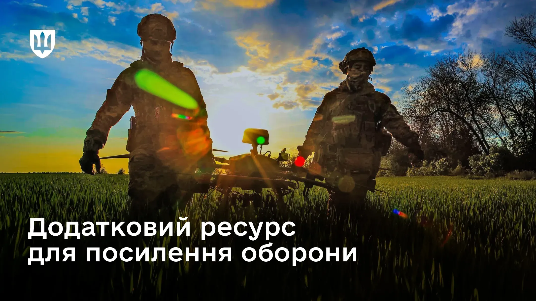 Двоє військовослужбовців несуть безпілотний комплекс полем на тлі заходу сонця