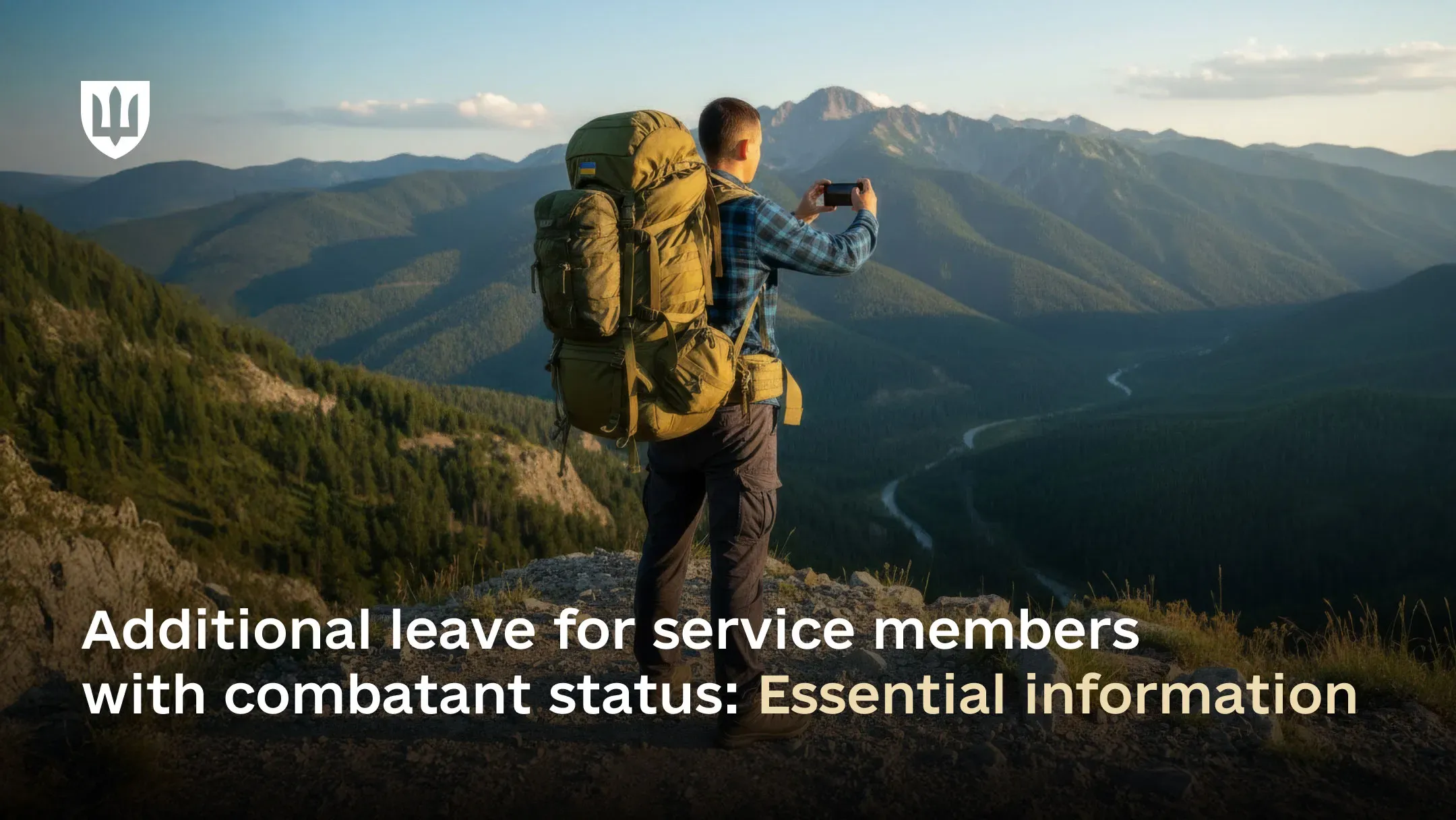 A hiker with a large backpack featuring a Ukrainian flag stands on a mountain peak, photographing the picturesque mountain landscape with a smartphone