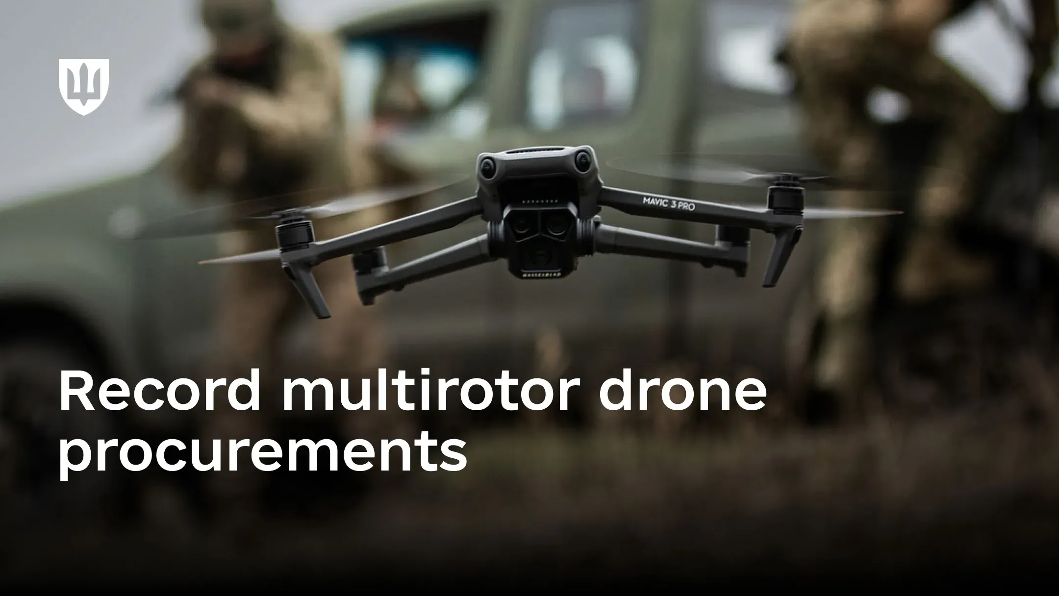 A Mavic 3 Pro multirotor drone in flight, with Ukrainian service members and a military vehicle in the background