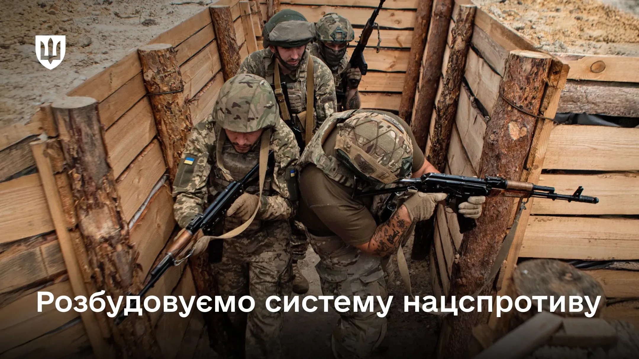 Чотири українські військовослужбовці у повному екіпіруванні та зі зброєю займають оборонні позиції у дерев'яному бліндажі