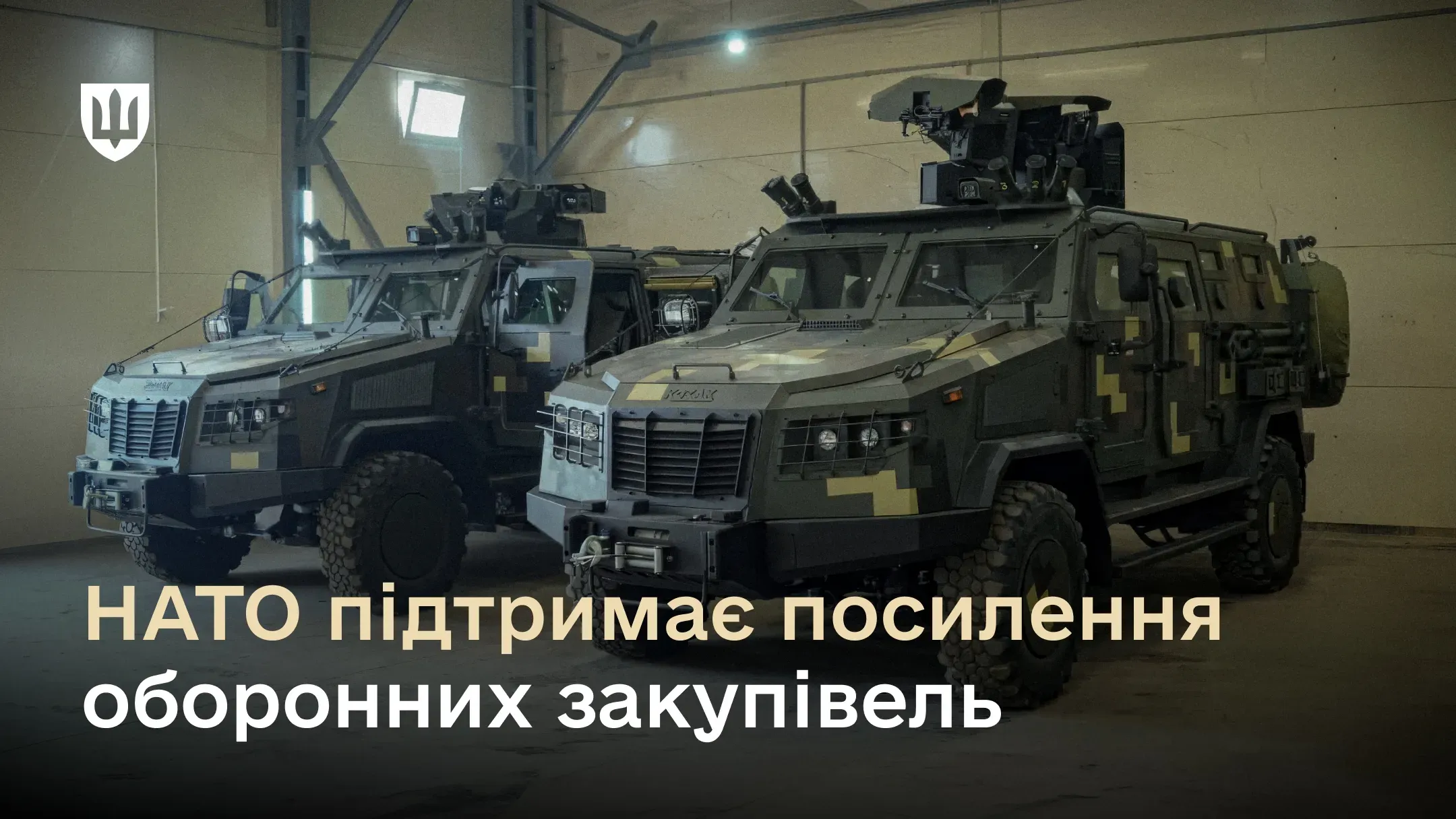 Два українські бронеавтомобілі «Козак-2М1» у піксельному камуфляжі з  дистанційно керованими бойовими модулями на даху стоять у великому ангарі