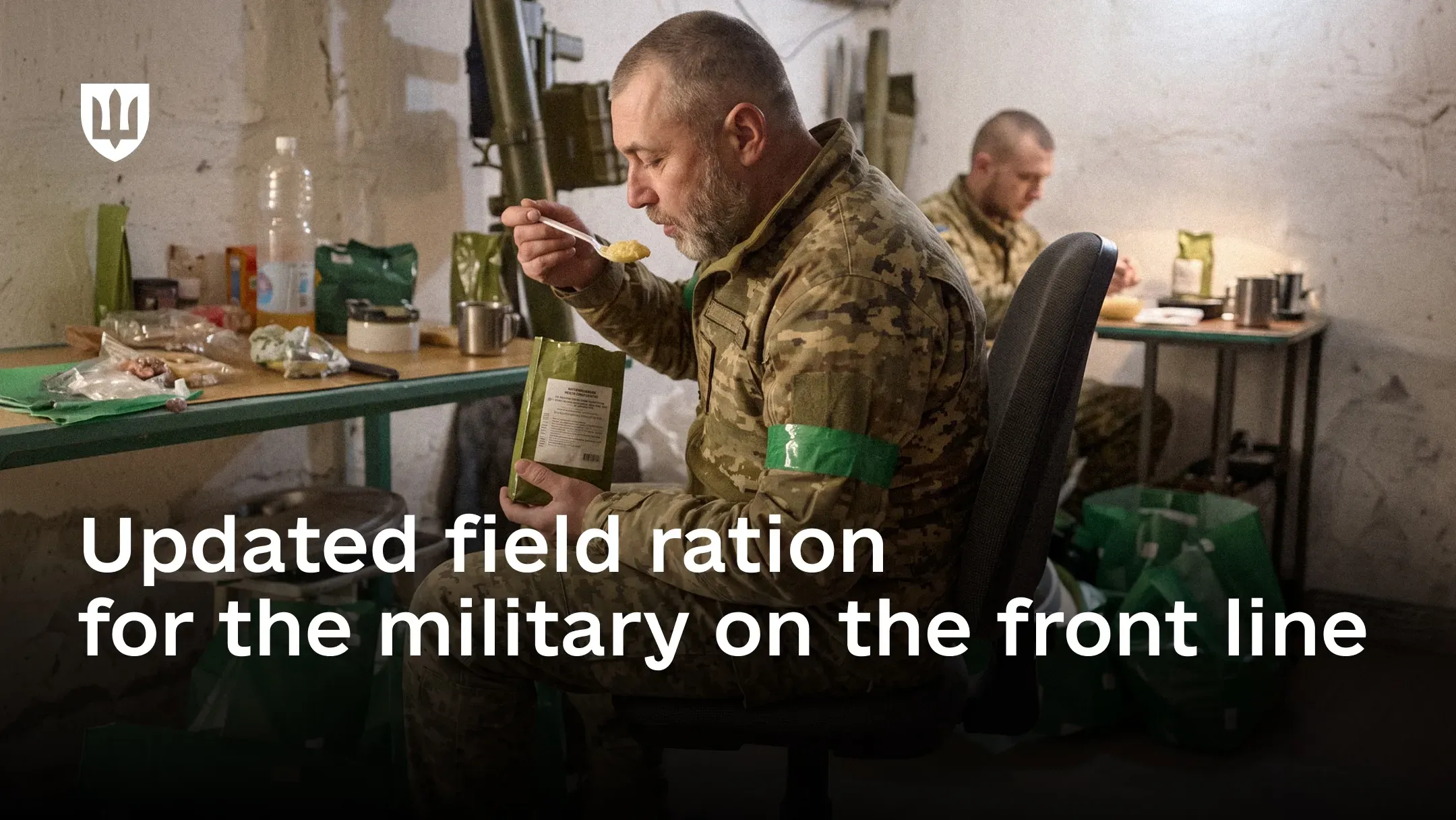 Ukrainian service member eats a ready-to-eat dish from a field ration pouch at a table, with another service member eating in the background. Text on the image: “Updated field ration for the military on the front line”