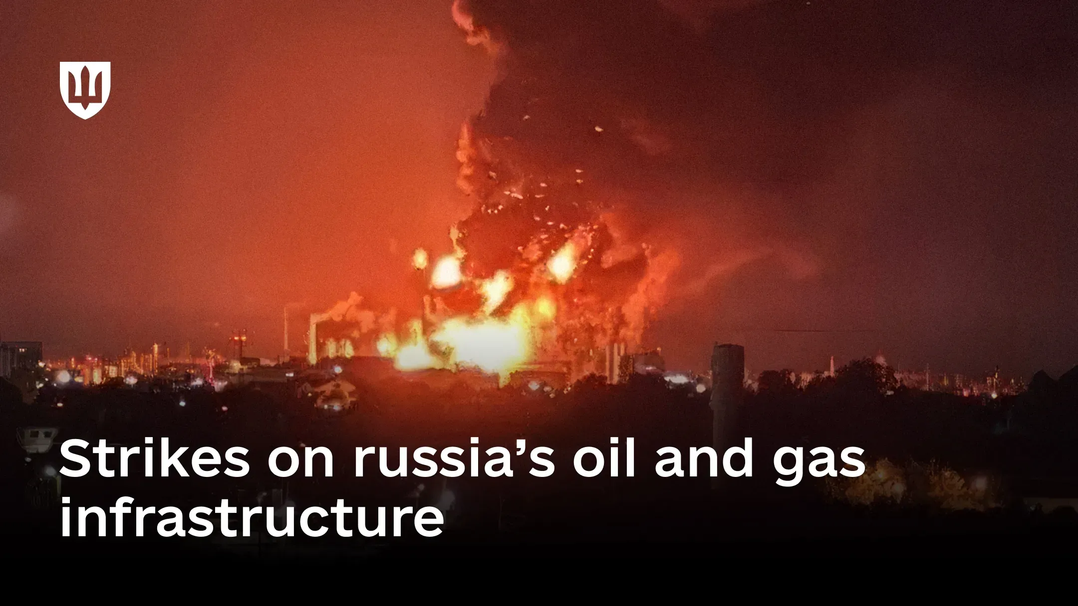 A plume of fire and smoke rises over an oil refinery against a nighttime urban backdrop
