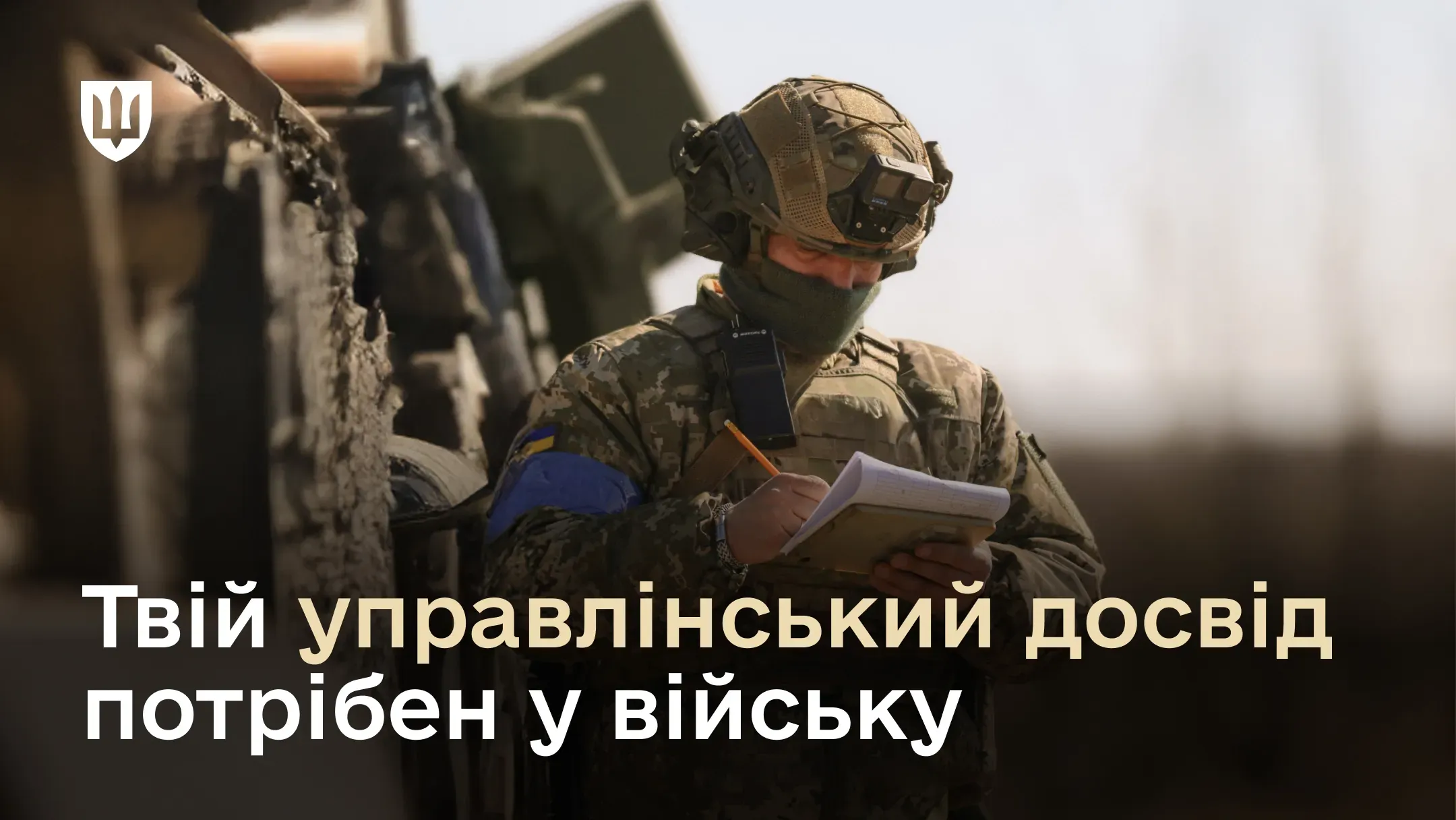 Військовий у повній бойовій екіпіровці та з рацією стоїть біля бронетехніки і зосереджено робить нотатки у блокноті. Поверх фото розміщено текст: «Твій управлінський досвід потрібен у війську».
