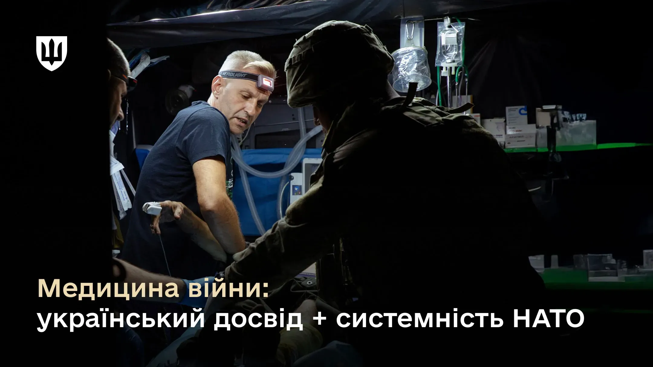 Фотографія всередині мобільного медичного госпіталю або реабілітаційного авто. Двоє українських військових медиків надають допомогу пораненому бійцю, який лежить на ношах.