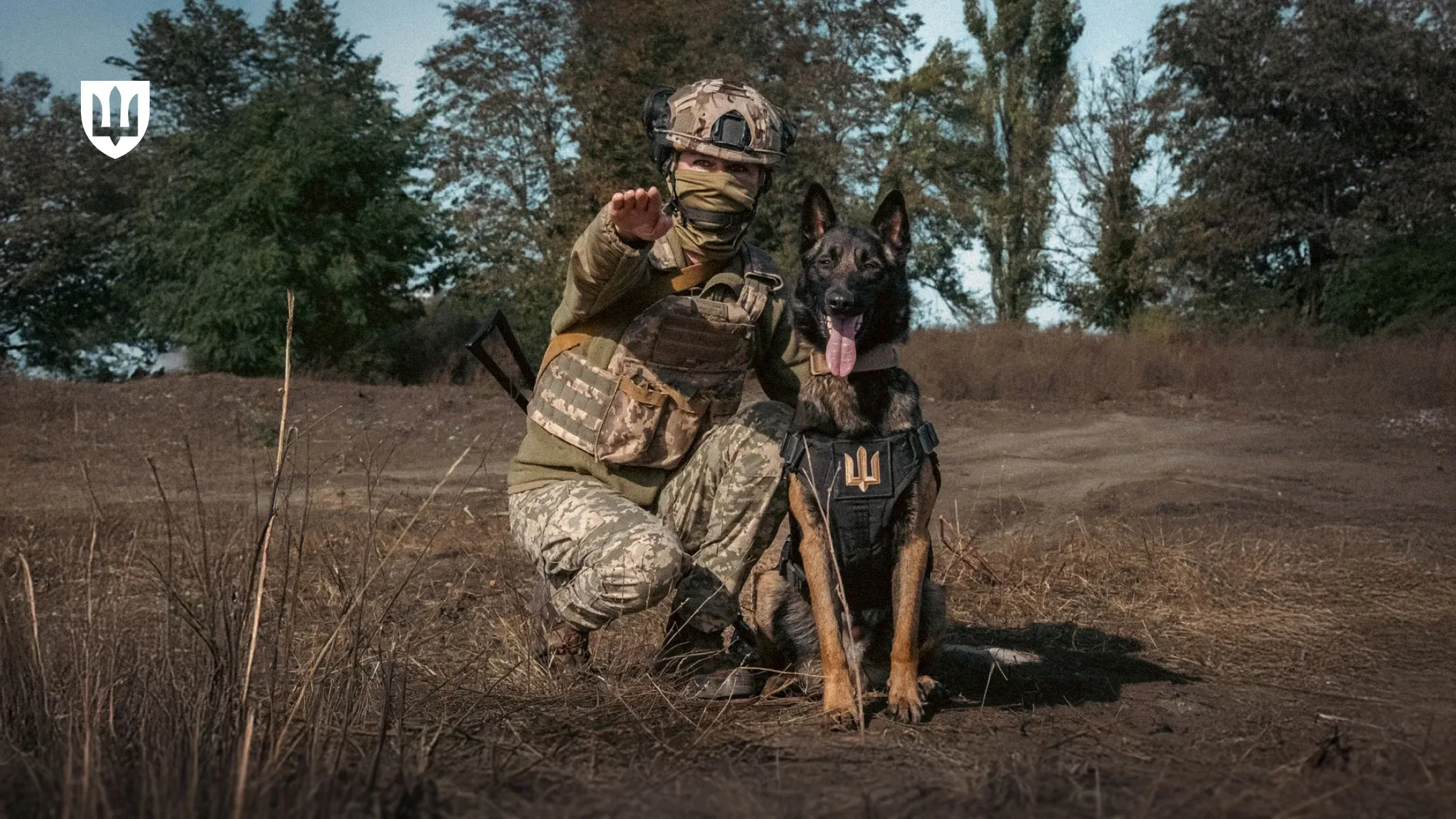 Військовий кінолог у камуфляжі біля собаки показує рукою вперед