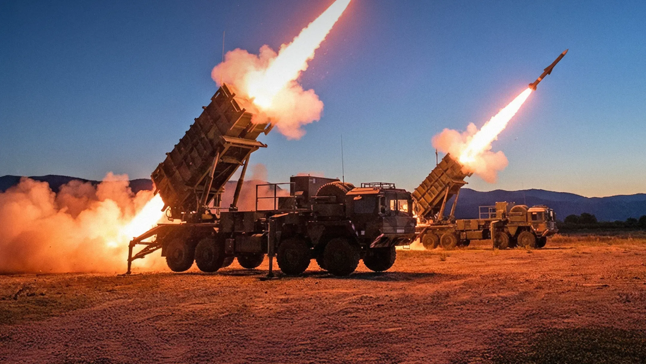 Two Patriot surface-to-air missile launchers fire a salvo of missiles in the evening